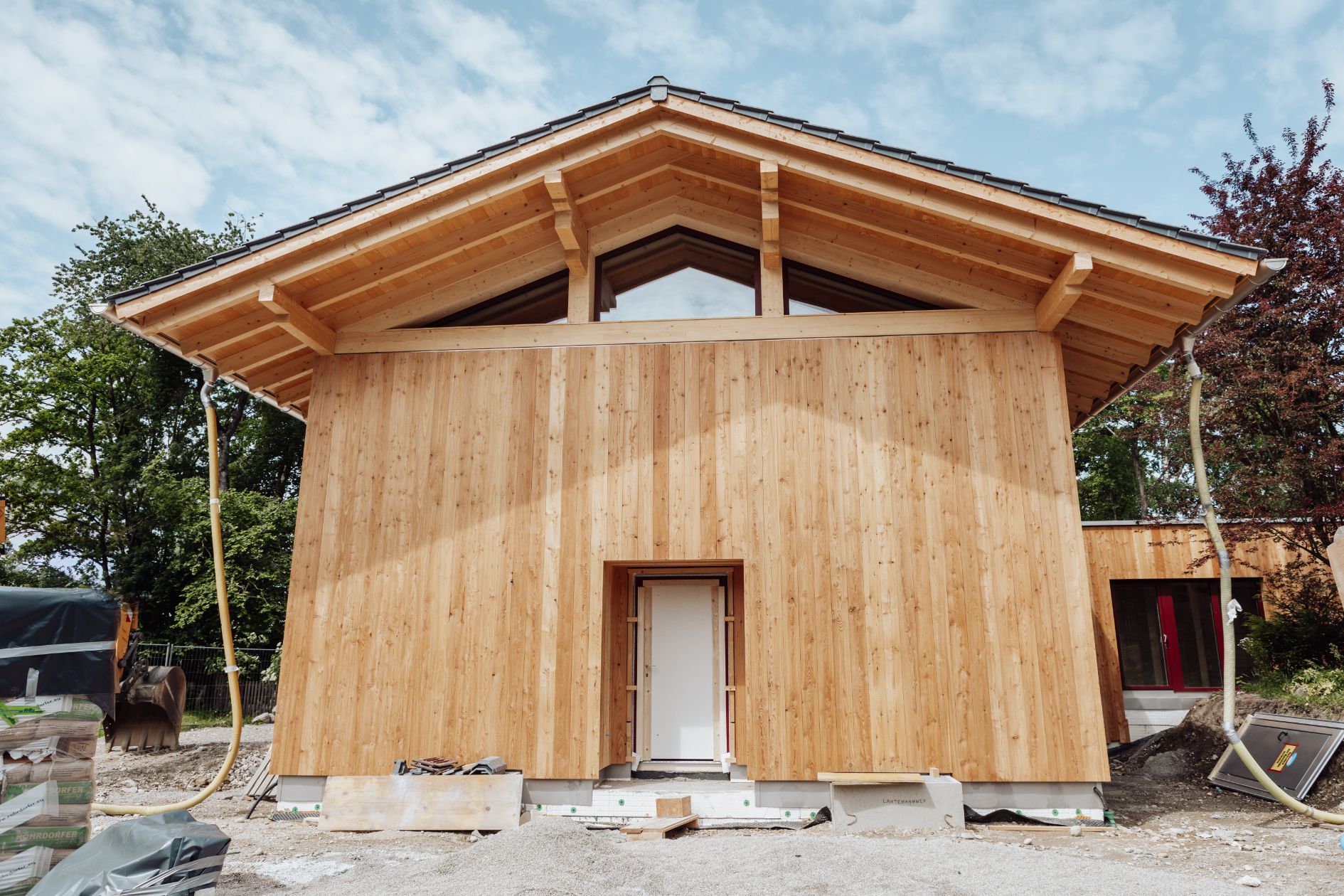 Frontansicht eines modernen Holzhauses mit sichtbarem Dachstuhl, Lärchenfassade und überdachtem Eingangsbereich.