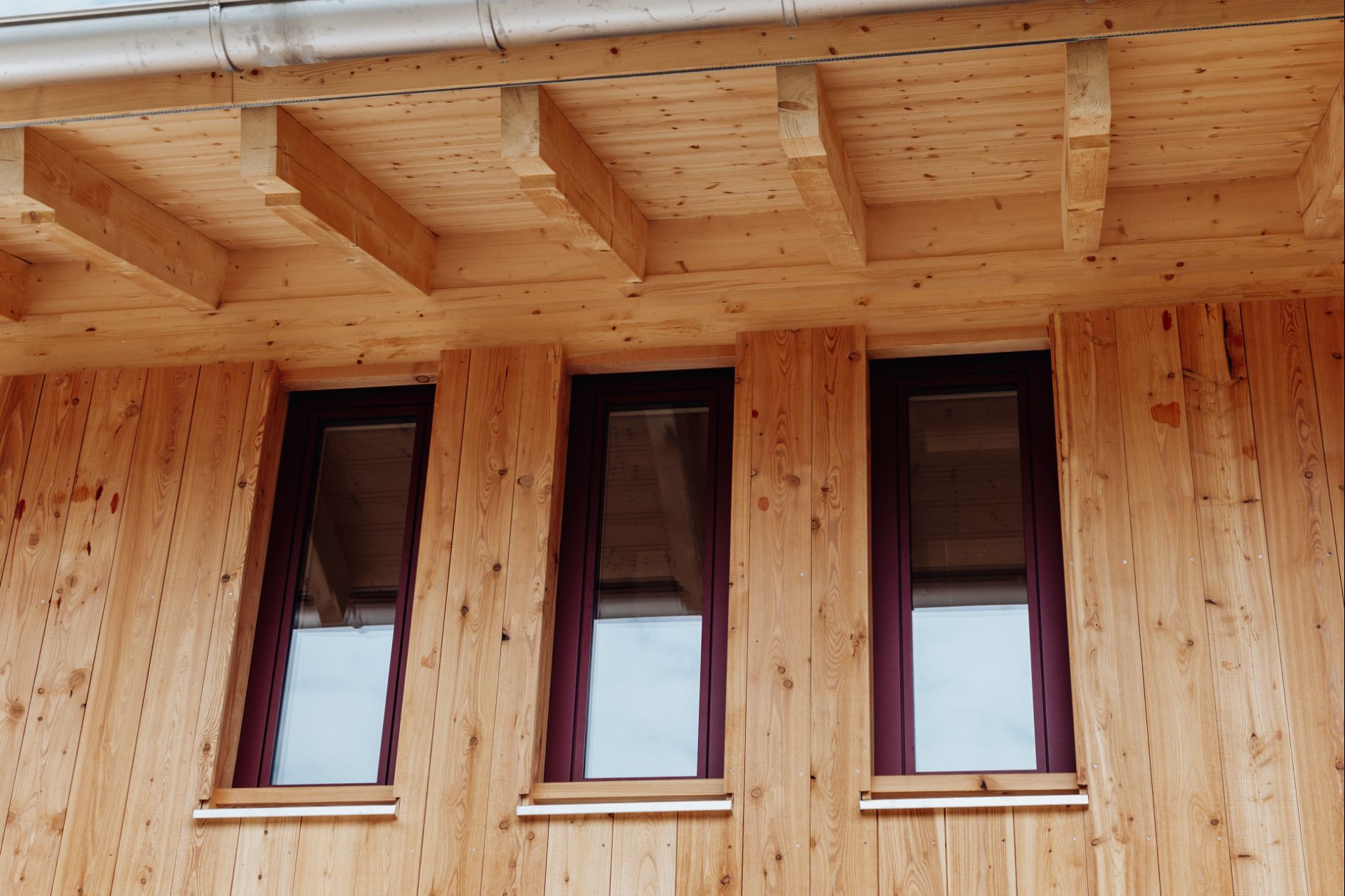 Fassade aus Lärchenholz mit markanten roten Fensterrahmen.
