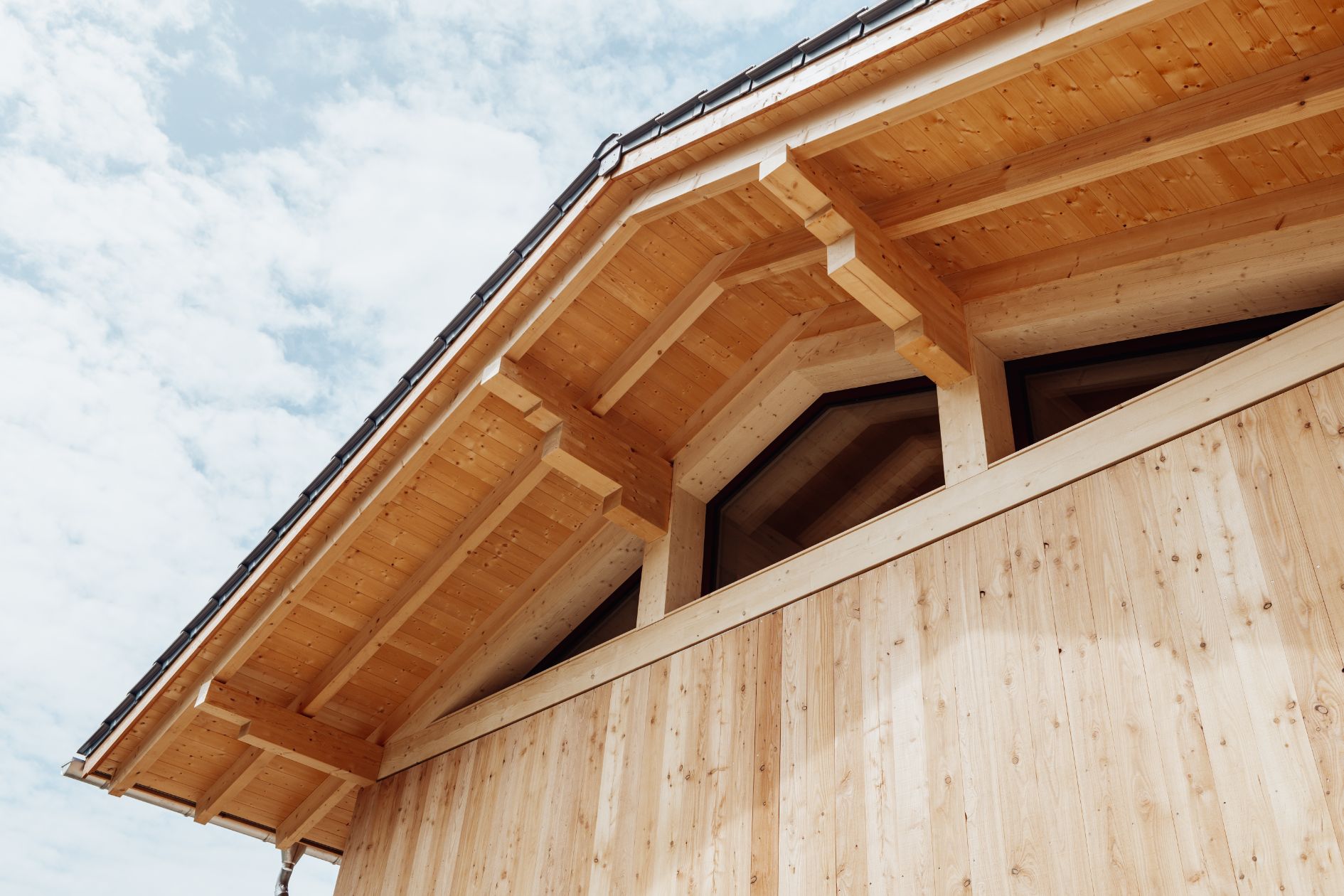 Sichtbarer Holz-Dachstuhl mit Lärchenfassade und dreieckigen Fenstern unter dem Giebel.