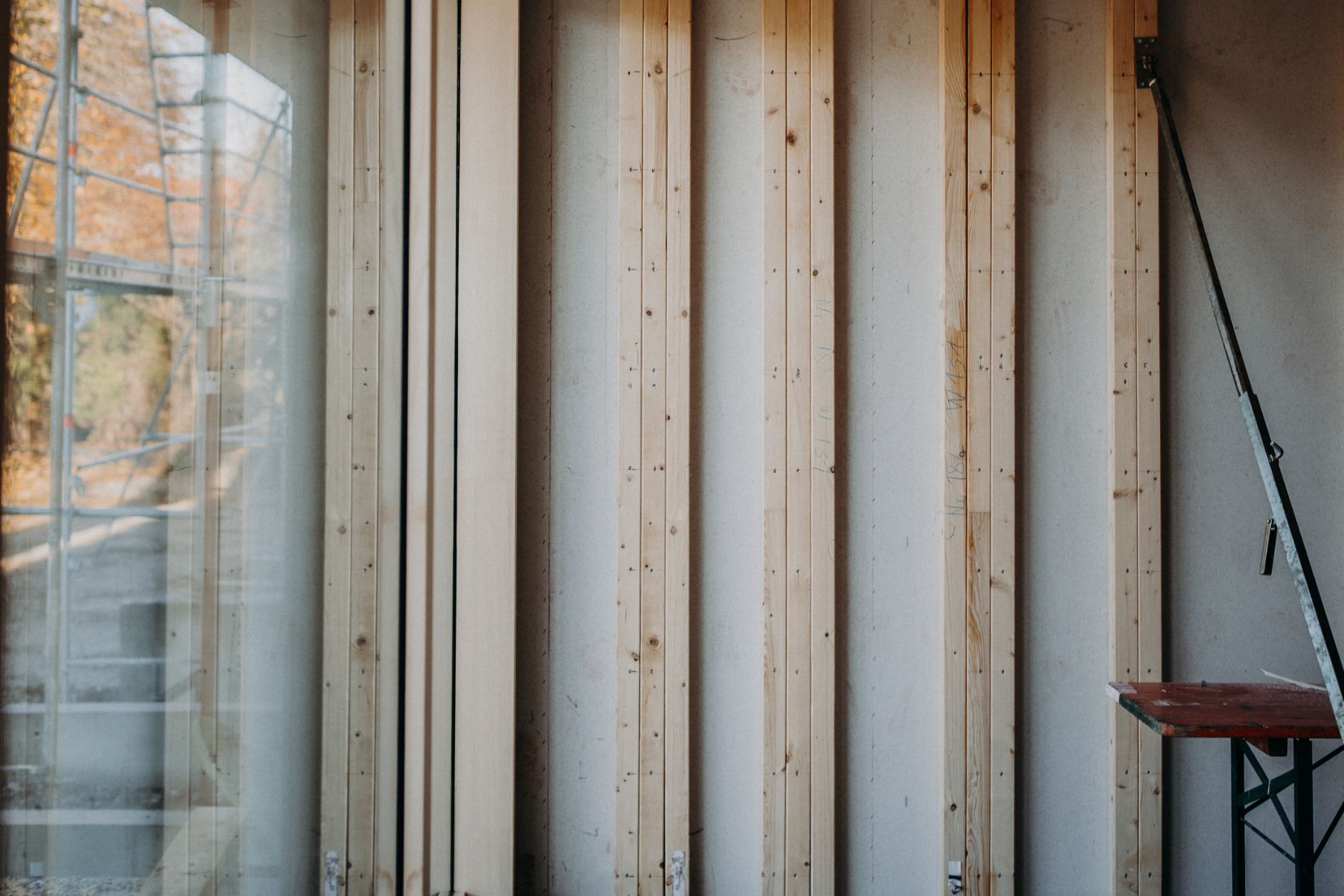 Innenansicht einer Wandkonstruktion mit sichtbaren Holzständern und großem Fensterbereich im Rohbau.