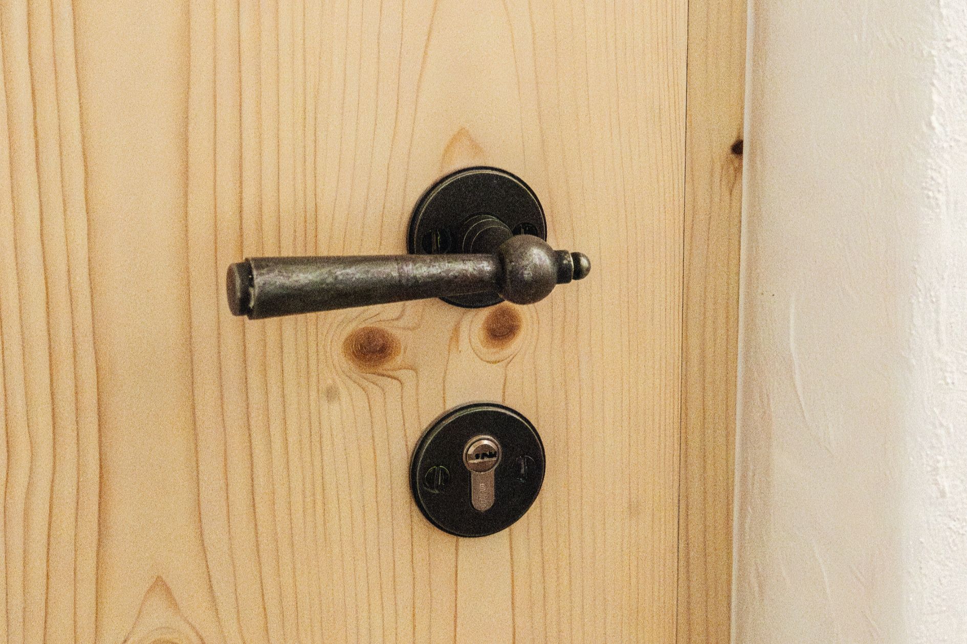 Detailaufnahme eines schwarzen, antiken Türgriffs mit passendem Schlüsselschild auf einer naturbelassenen Holztür.