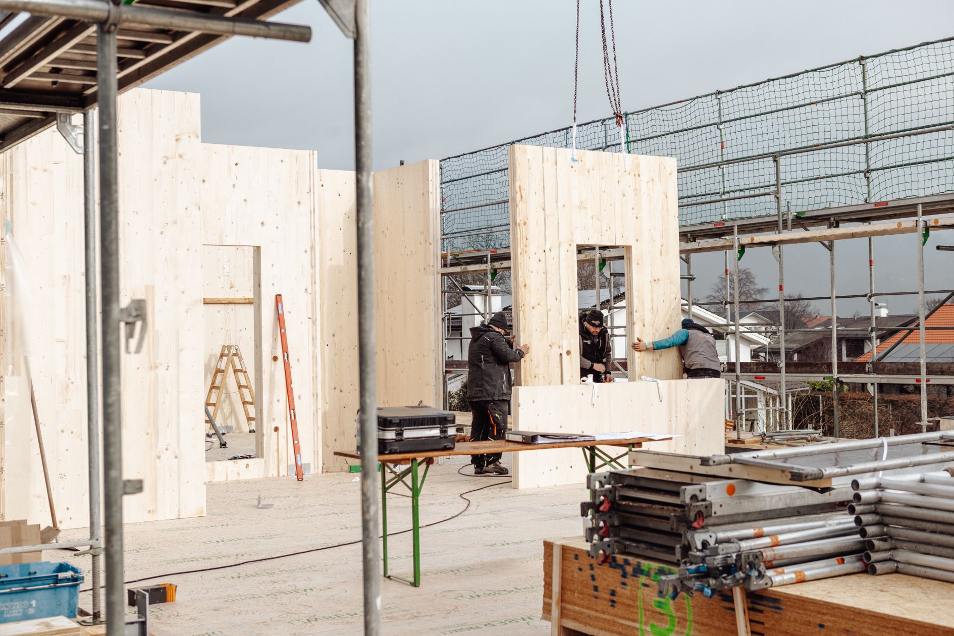 Handwerker richten CLT-Wandelement mit Fensteröffnung auf Baustelle aus
