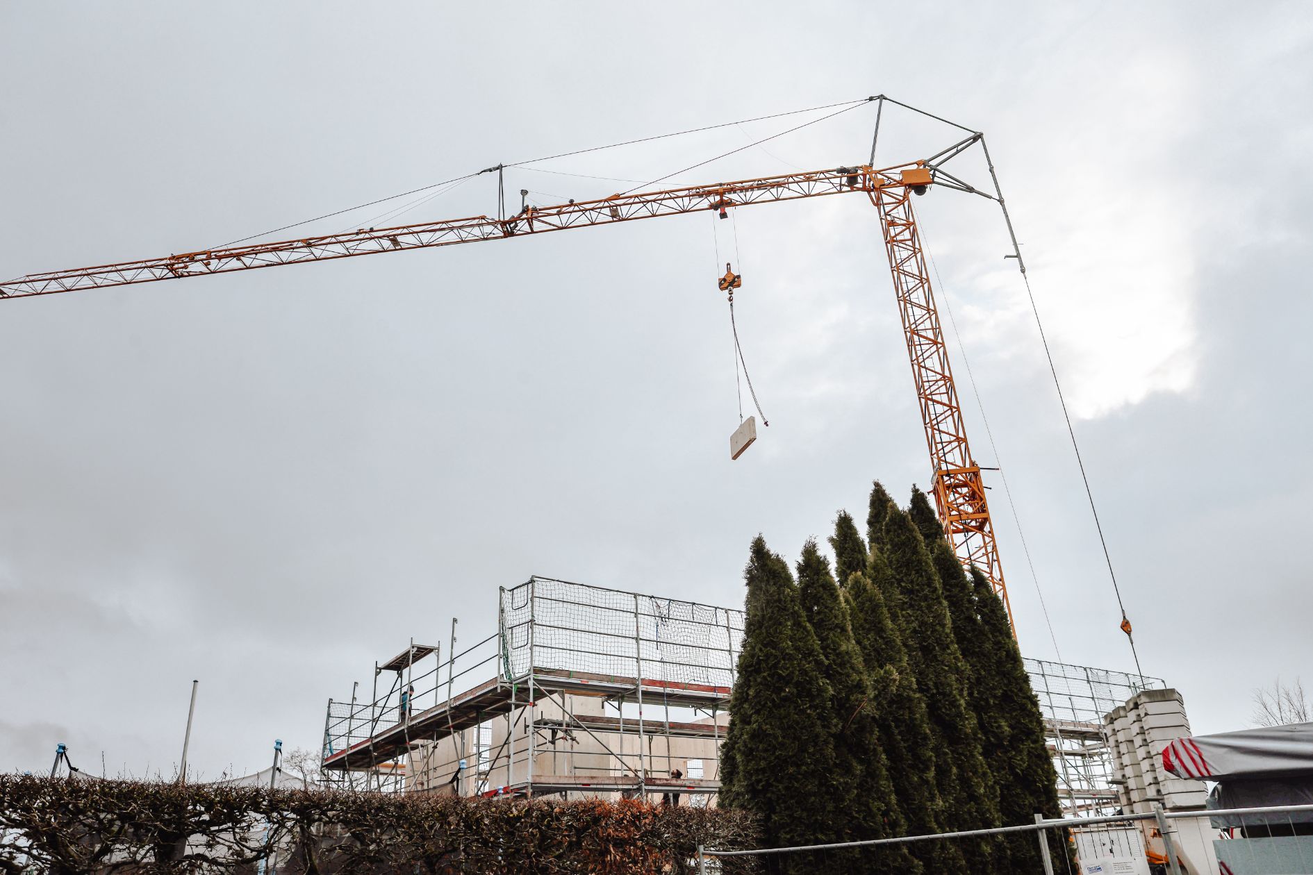 Ein Baukran hebt eine Holzplatte über eine eingerüstete Baustelle.