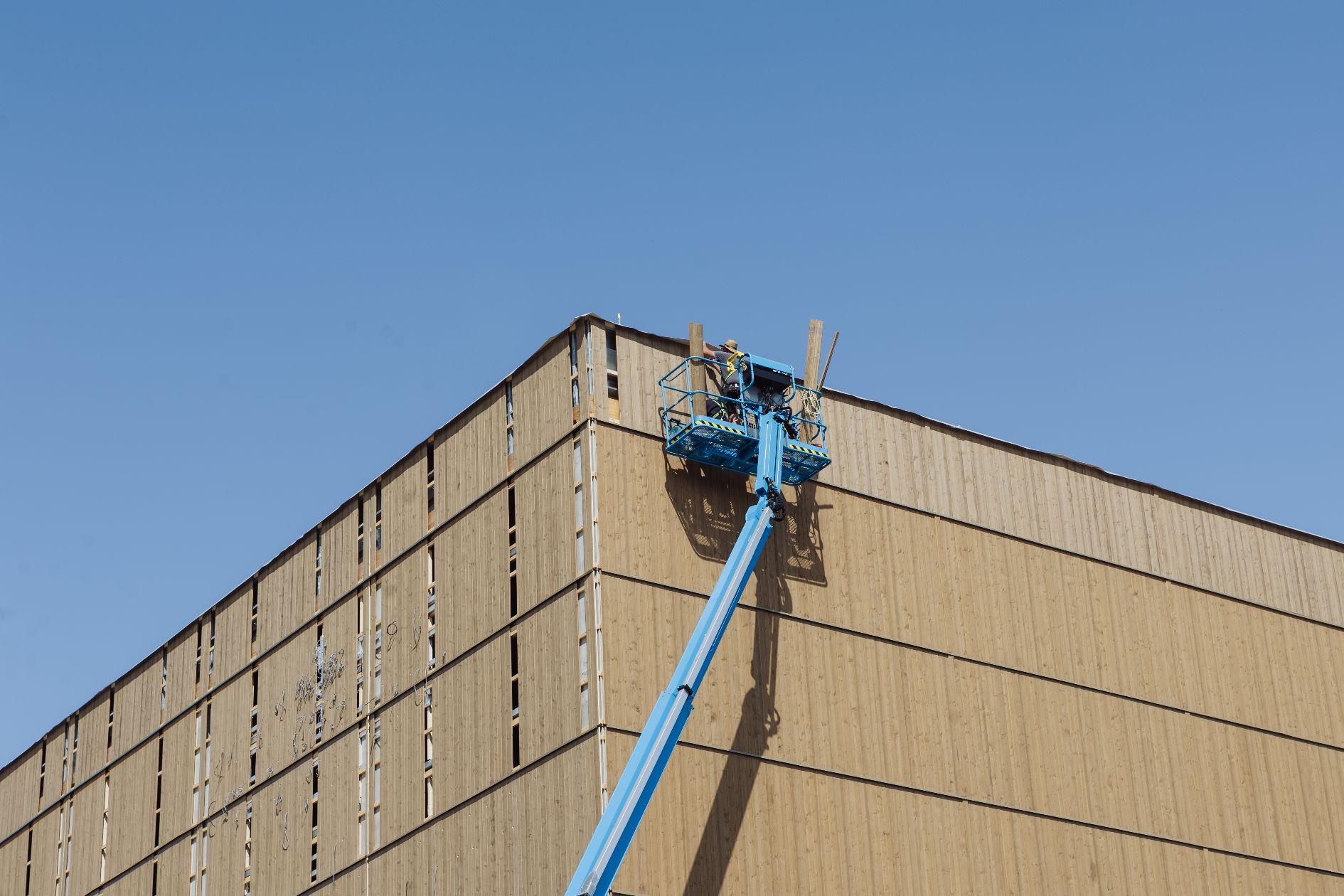 Arbeiter montiert obere Holzpaneele einer hohen Gebäudefassade