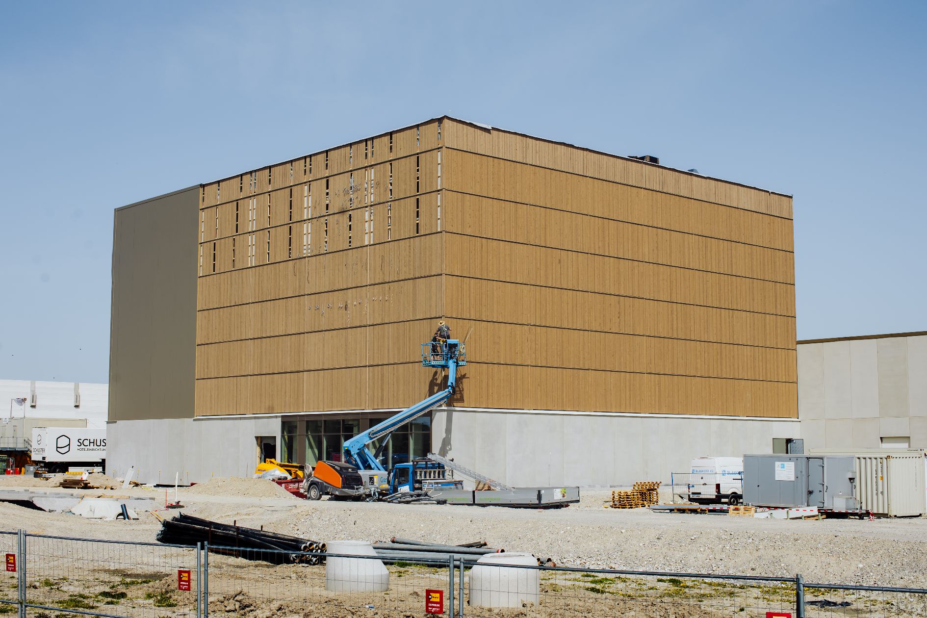Holzverkleidetes Industriegebäude in Bauphase mit Arbeitsbühne und Baustellenausstattung