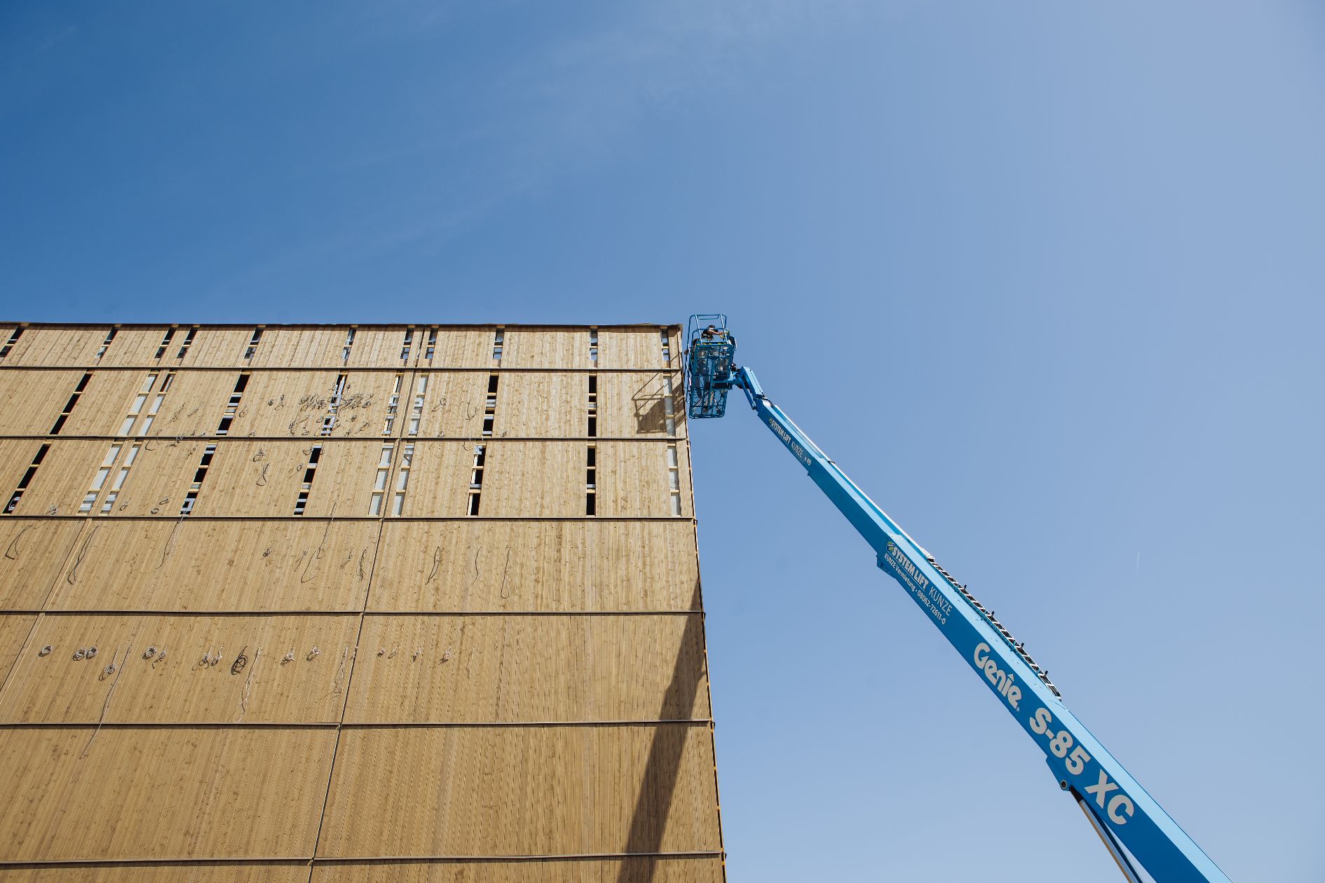 Arbeitsbühne in großer Höhe an der Holzfassade eines Industriegebäudes