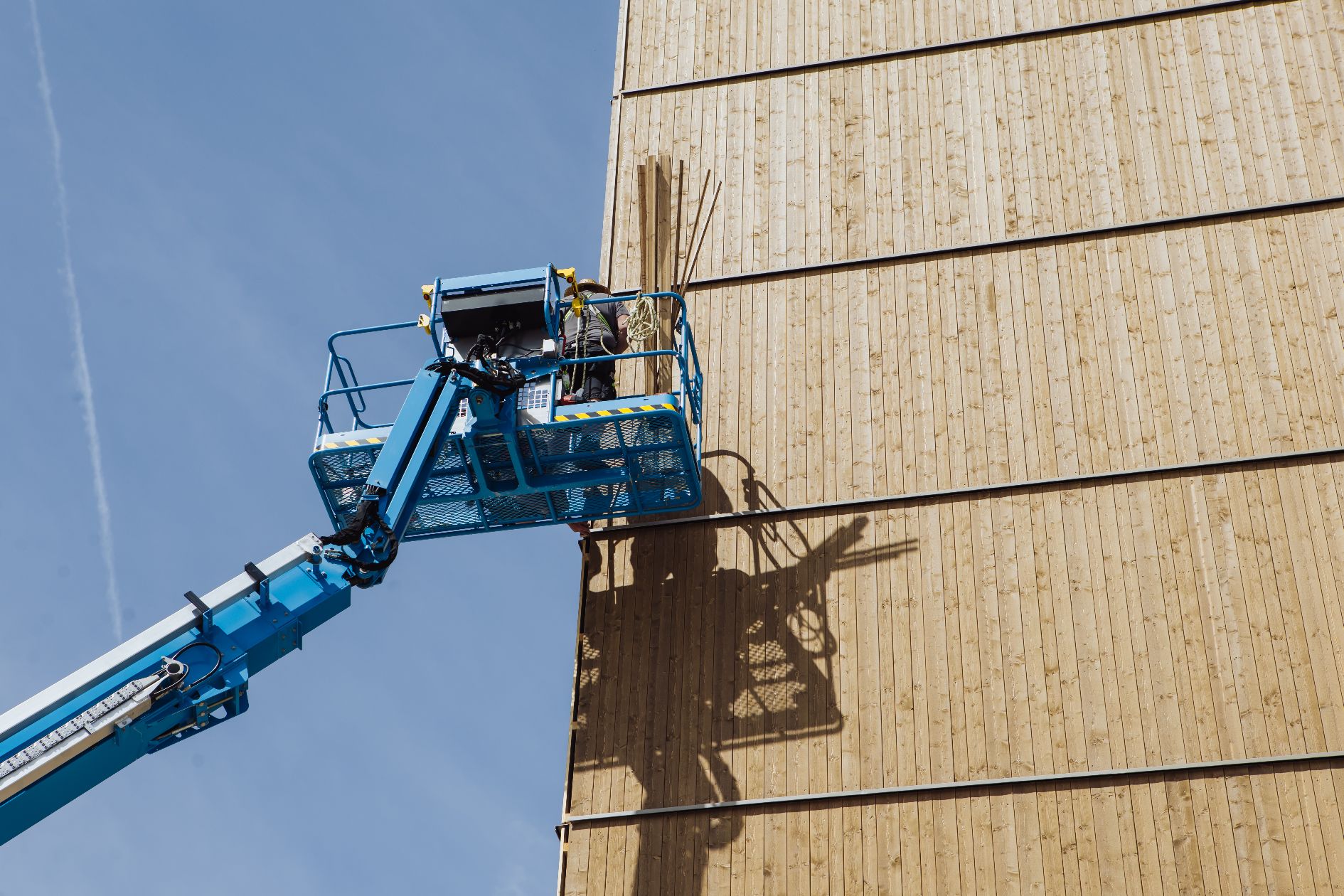 Hebebühne mit Arbeitern in großer Höhe an einer Holzfassade