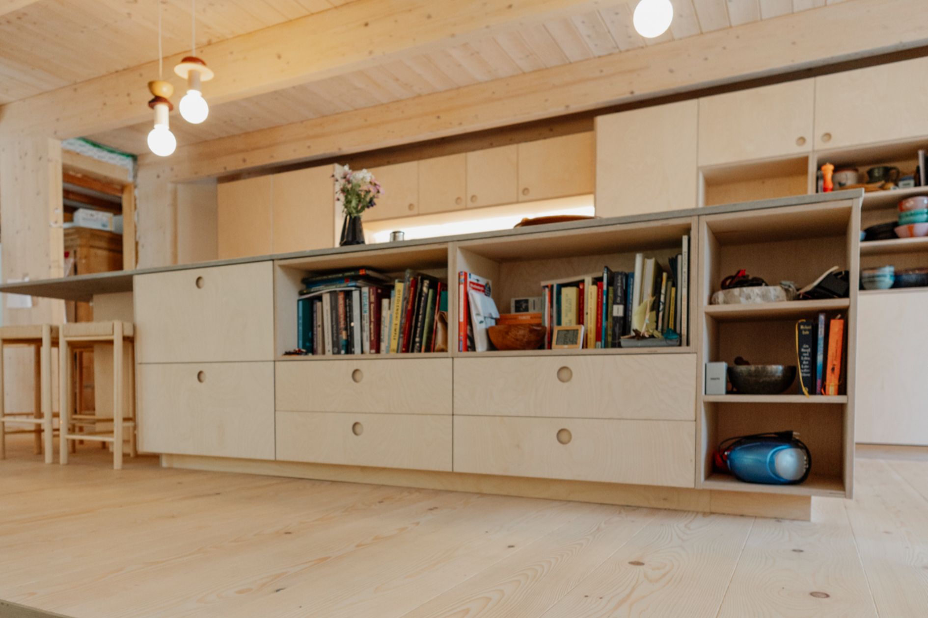 Helle Wohnküche mit Bücherregal in der Kochinsel und Tannenboden.