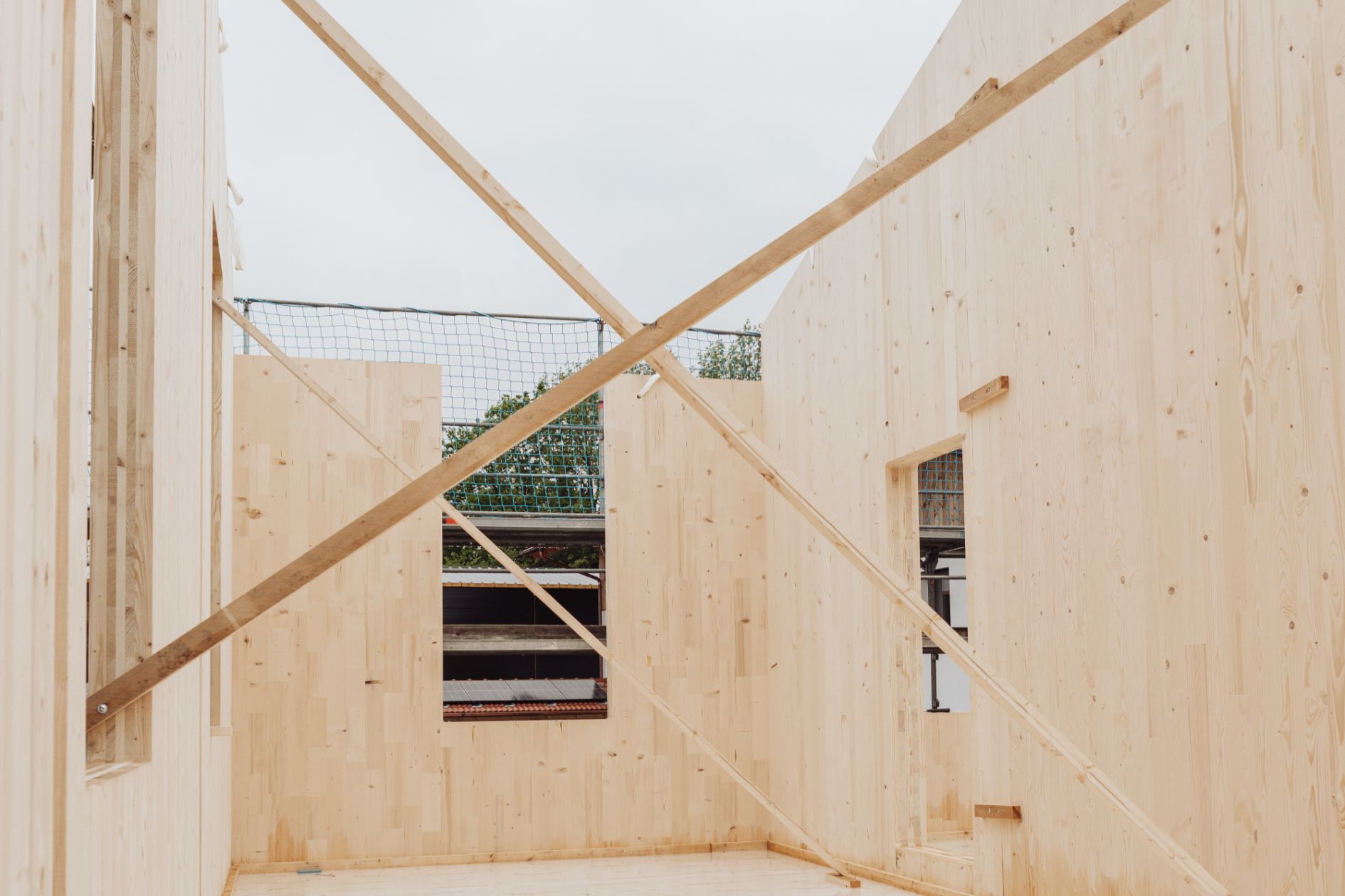 Innenansicht eines Holzrohbaus mit abgestützten Brettsperrholzwänden und Fensteröffnungen.