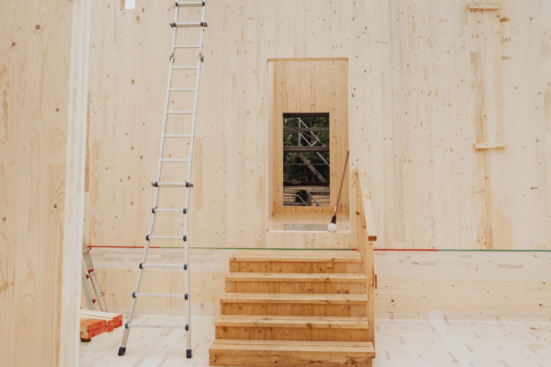 Holztreppe und Leiter im Rohbau aus Brettsperrholz mit Fensteröffnung.