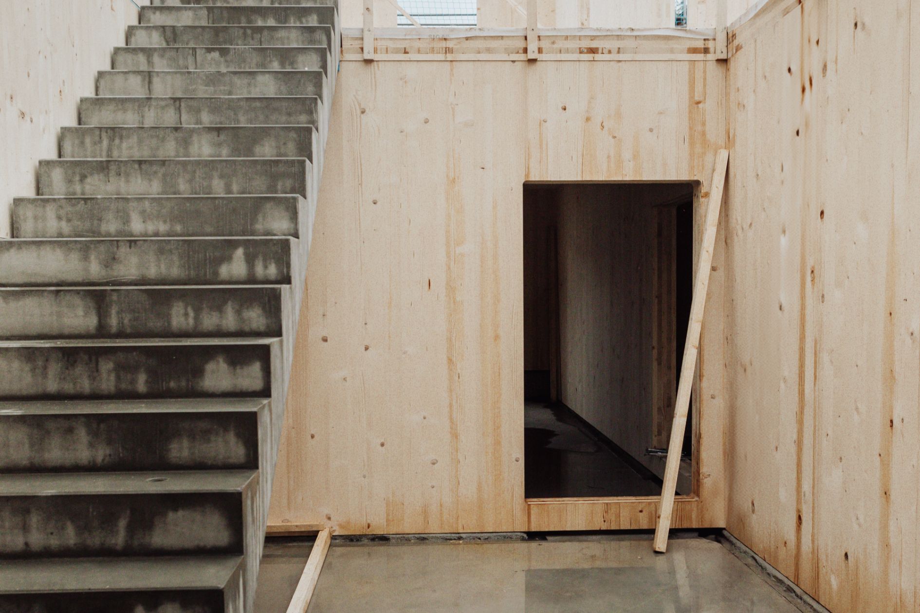 Betontreppe im Rohbau mit Holzverkleidung und Durchgang.