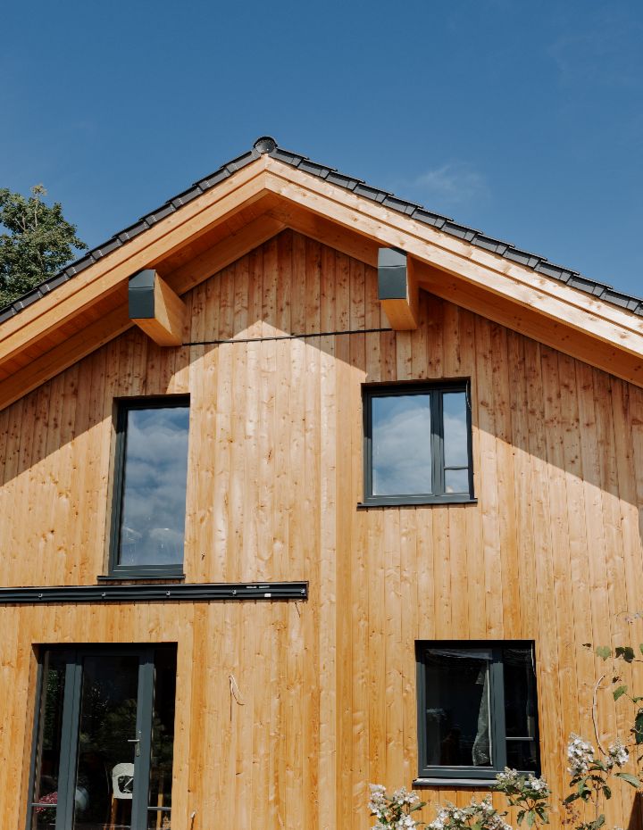 Frontansicht eines Einfamilienhauses mit Holzverkleidung und anthrazitfarbenen Fenstern