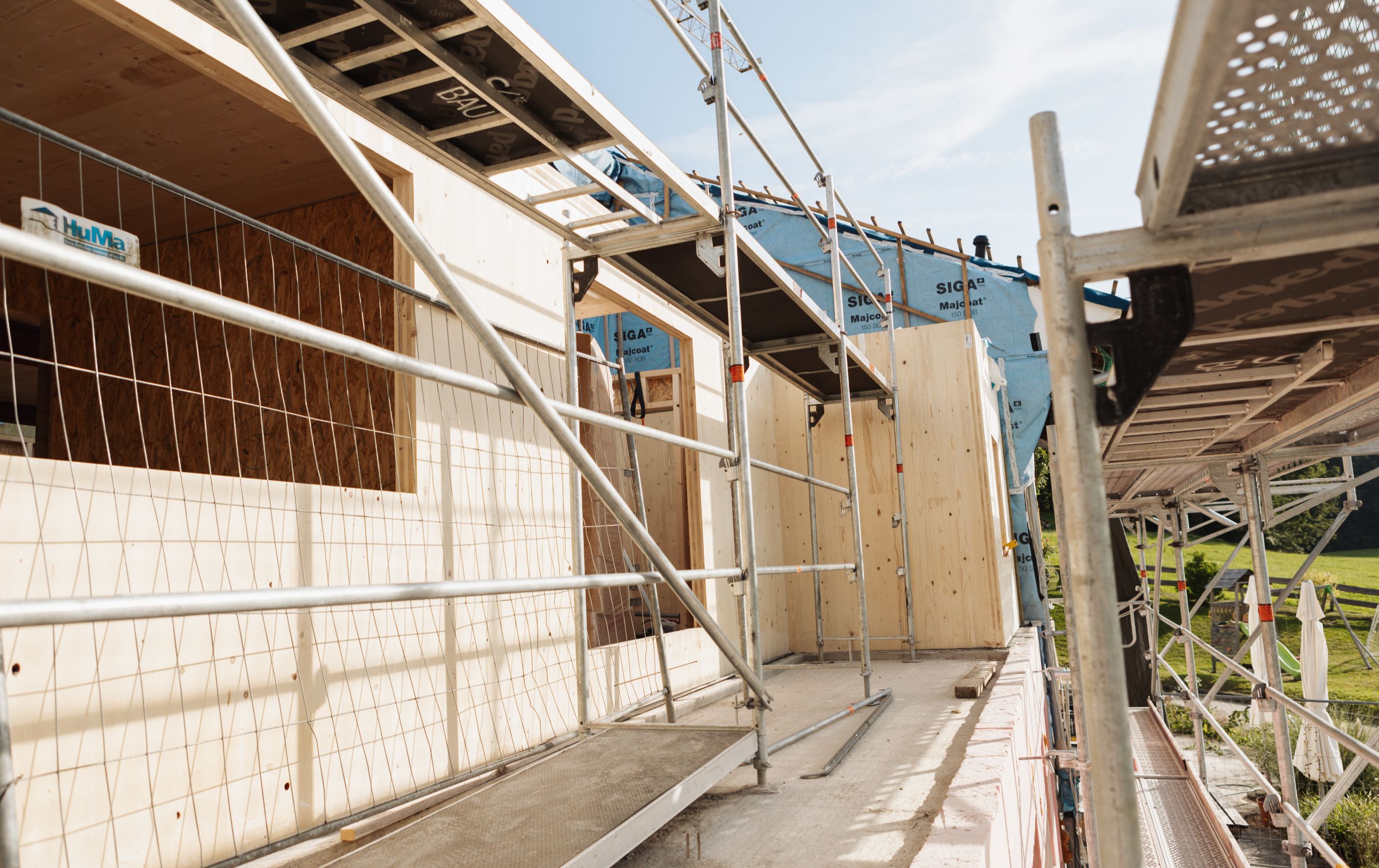 Außenansicht einer eingerüsteten Holzbaustelle mit montierten Wandplatten und sichtbaren Fensteröffnungen