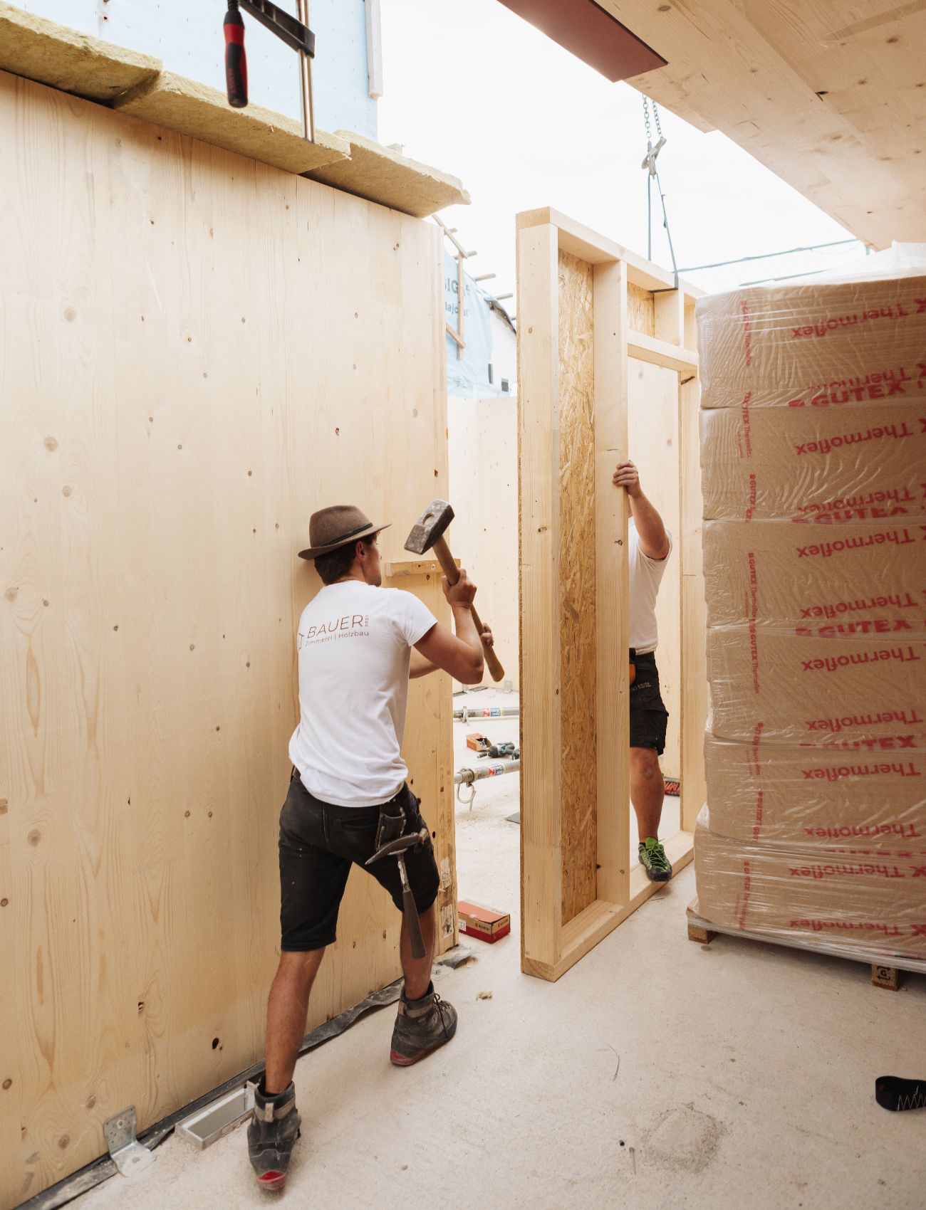 Zwei Handwerker montieren eine Holzwand auf einer Baustelle.