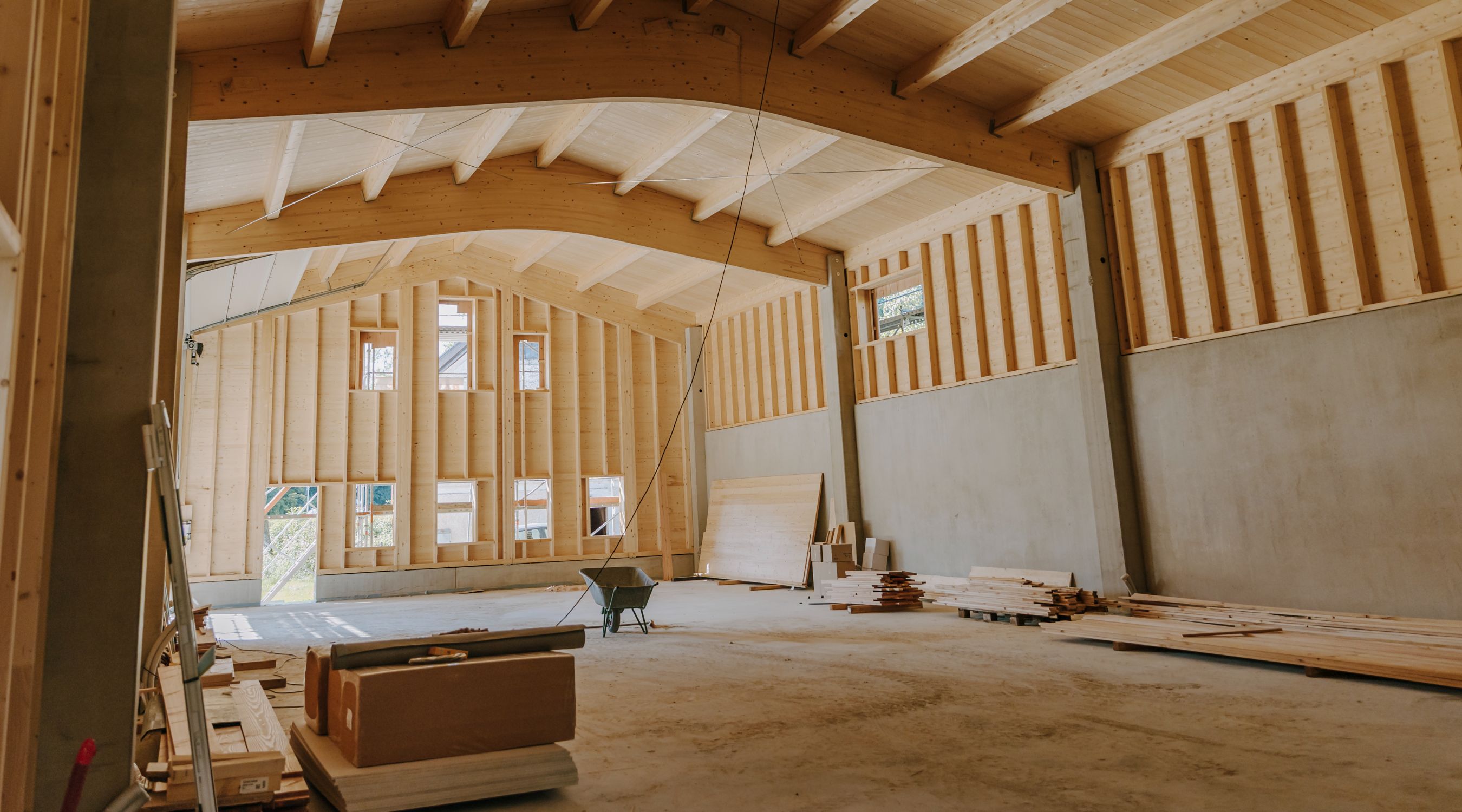 Innenansicht einer Holzbau-Halle im Rohbau mit Brettschichtholzträgern, Holzrahmenwänden und Betonbasis