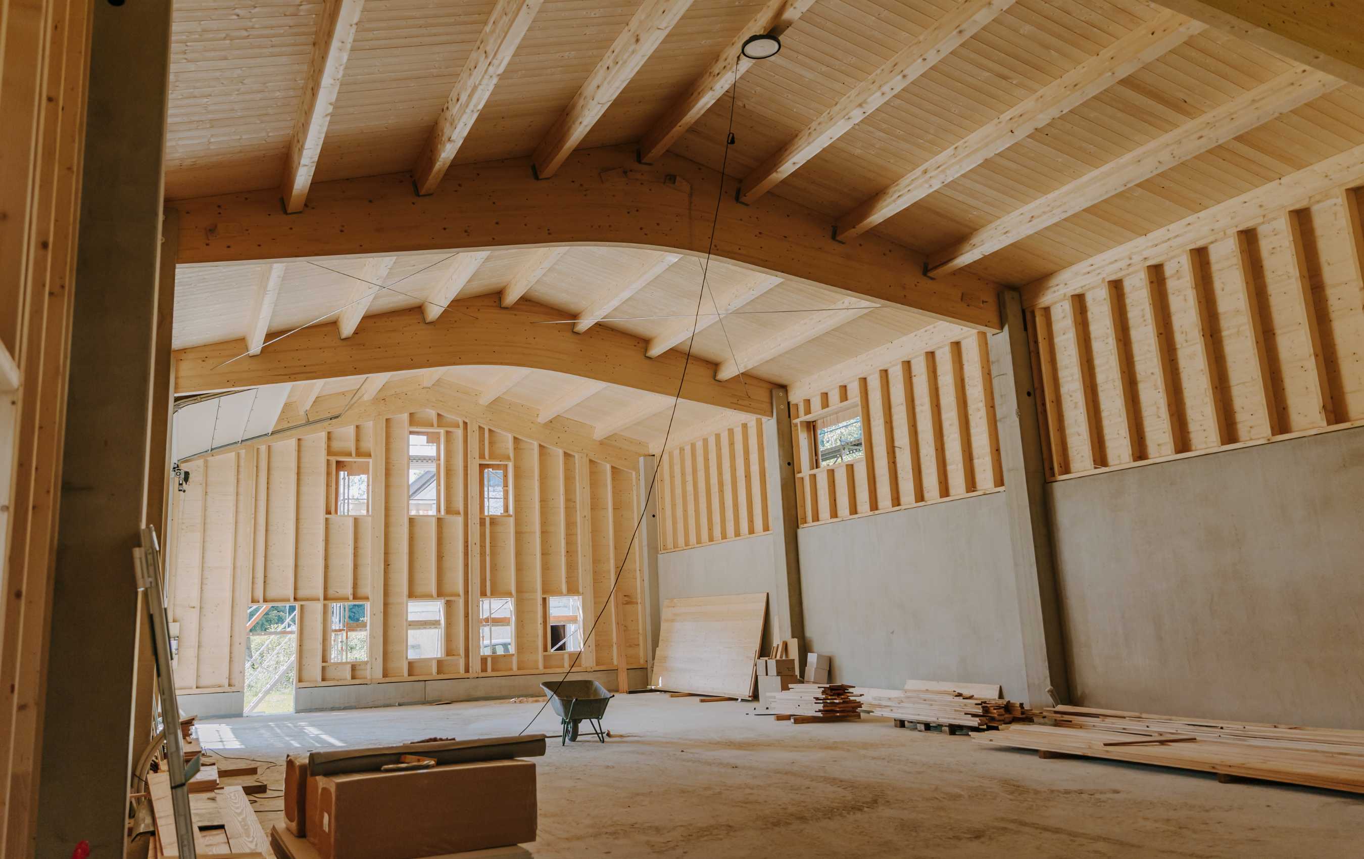 Innenraum eines Neubaus mit sichtbarer Holztragkonstruktion, hohen Decken und unverkleideten Wänden