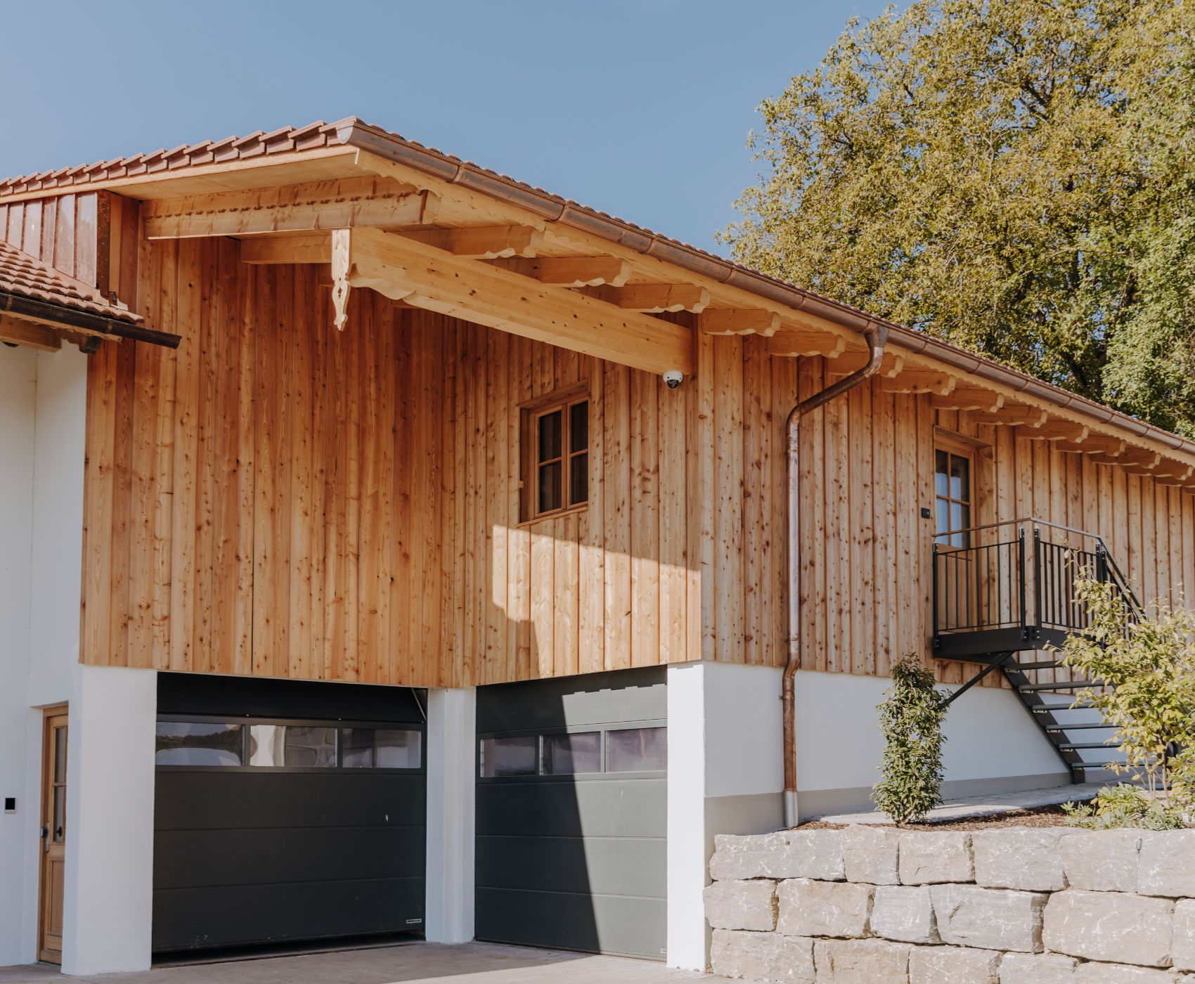 Modernes Wohnhaus mit Holzfassade, Doppelgarage, Außentreppe und begrüntem Vorbereich