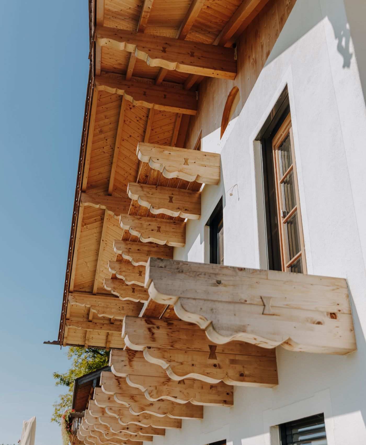 Hausfassade mit weißem Putz, hölzernen Fensterläden und dekorativ geschnitzten Holzelementen