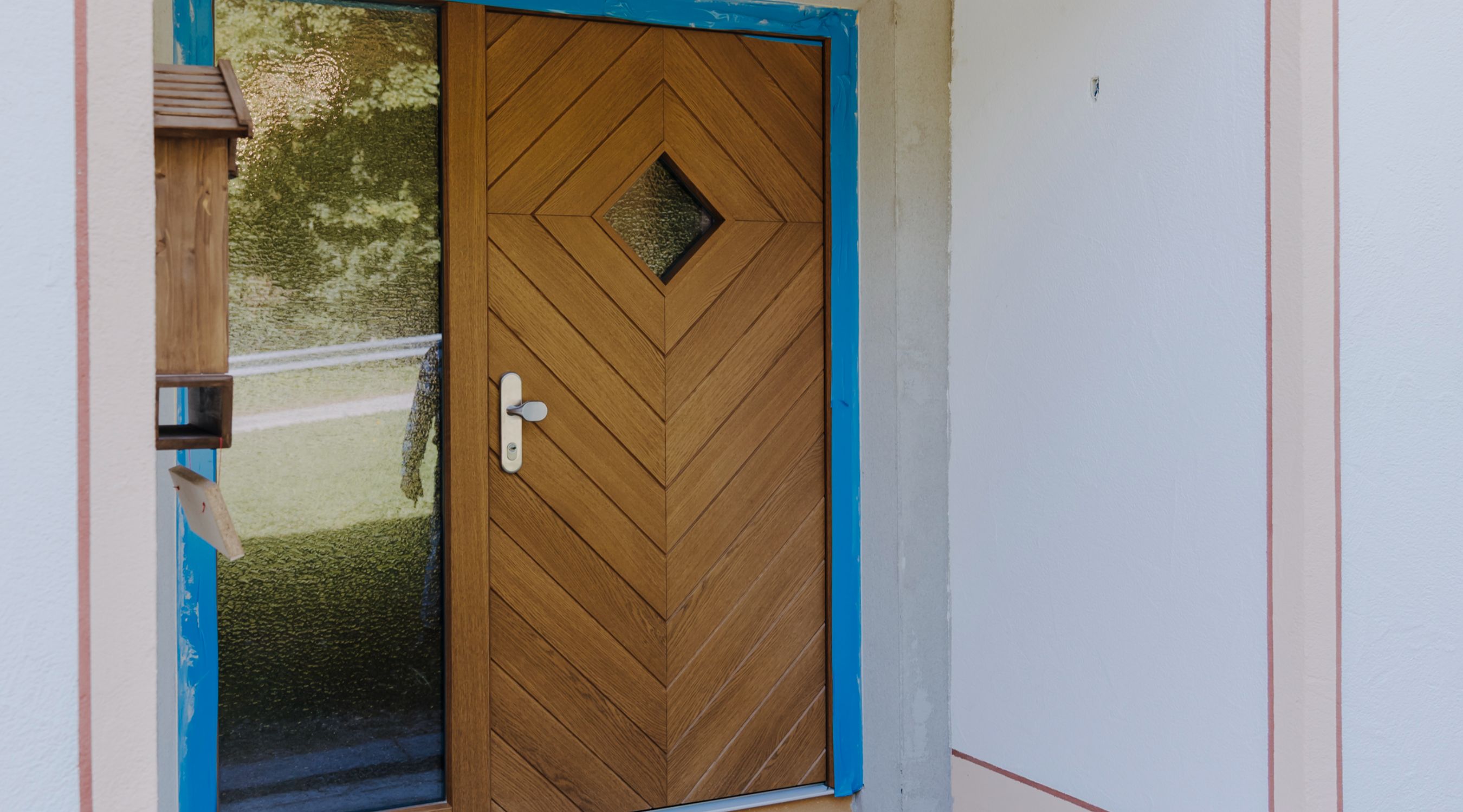 Eingangstür aus Holz mit Fischgrätmuster, kleinem rautenförmigen Fenster und Glas-Seitenteil