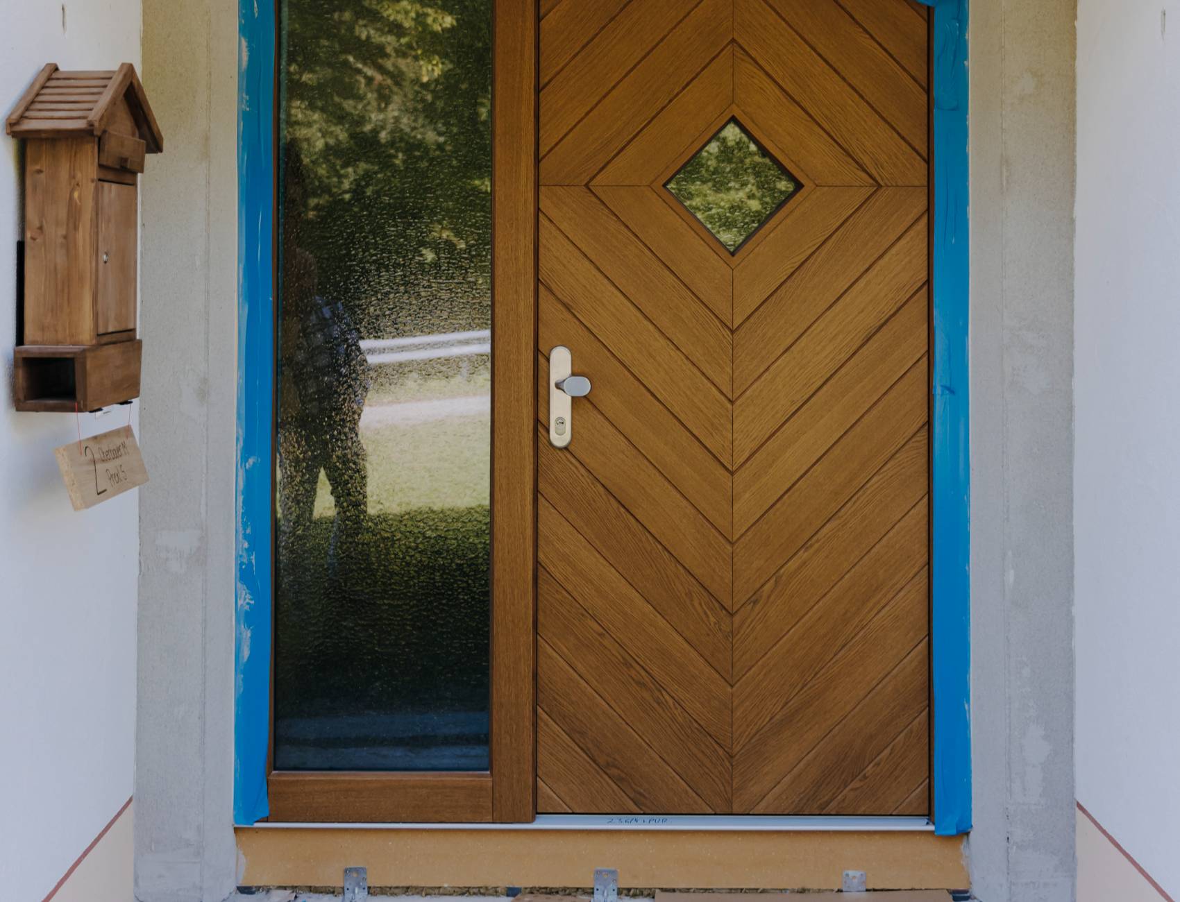 Detailaufnahme einer Holztür mit rautenförmigem Milchglasfenster und schwarzem Türgriff