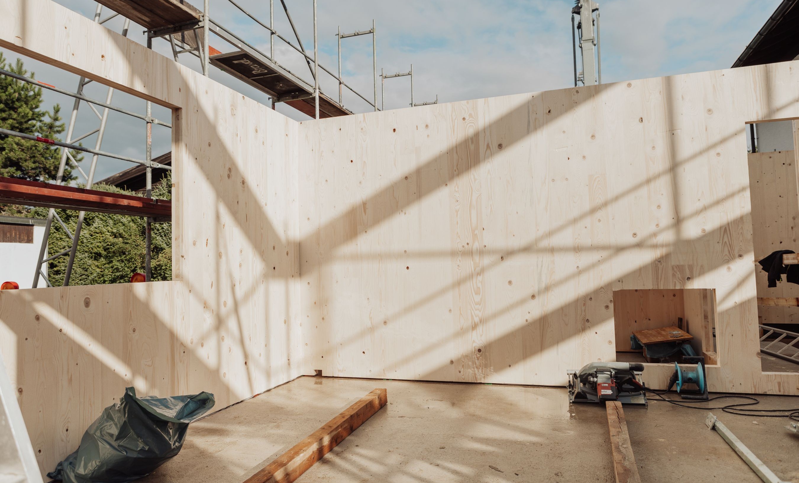 Montierte Brettsperrholzwände im Anbau an ein Bestandsgebäude, vorbereitete Wandöffnungen und Baustelleneinrichtung im Rohbauzustand.