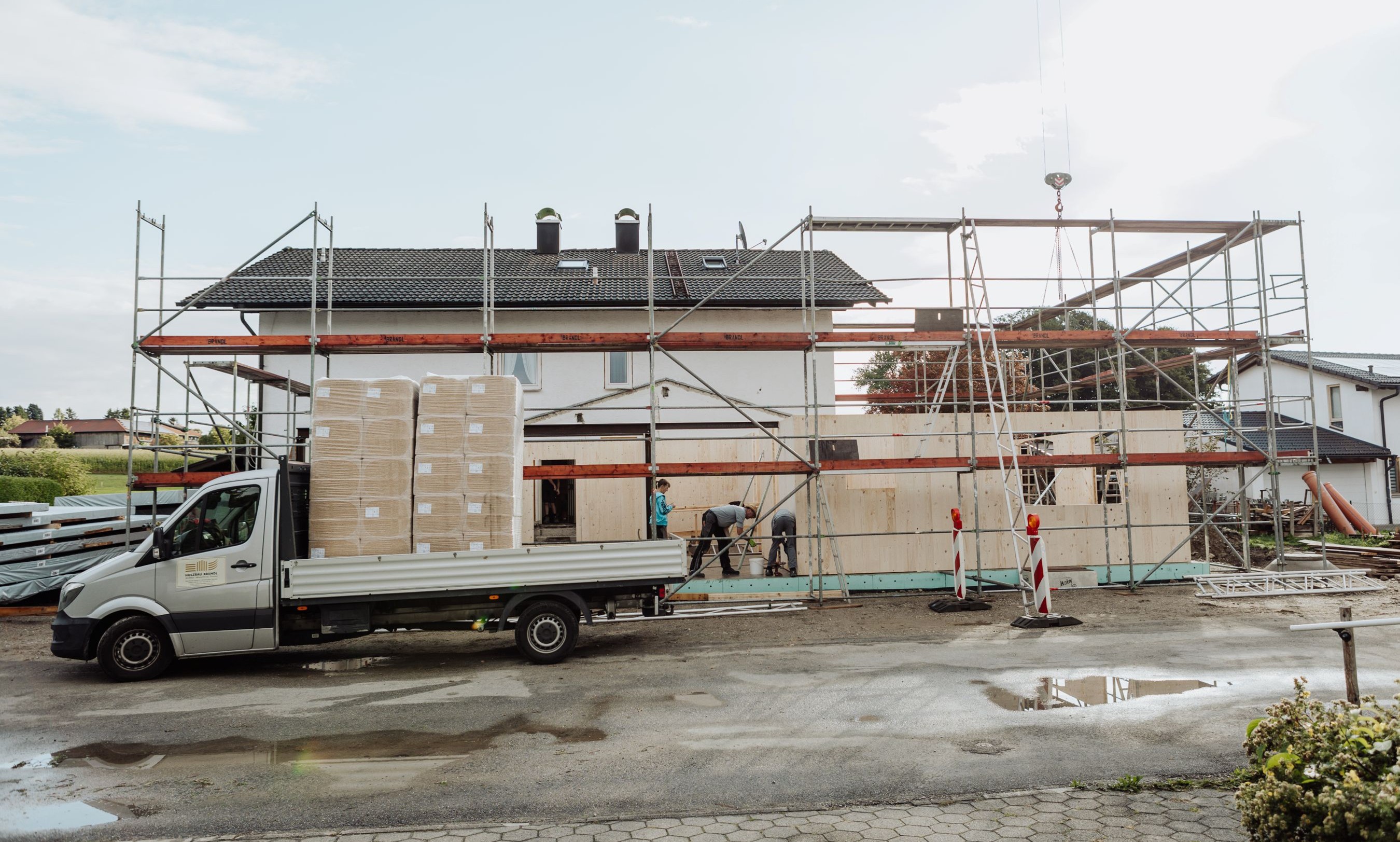 Außenansicht der Baustelle mit montierten Brettsperrholzwänden des Anbaus und Baustelleneinrichtung im Vordergrund.