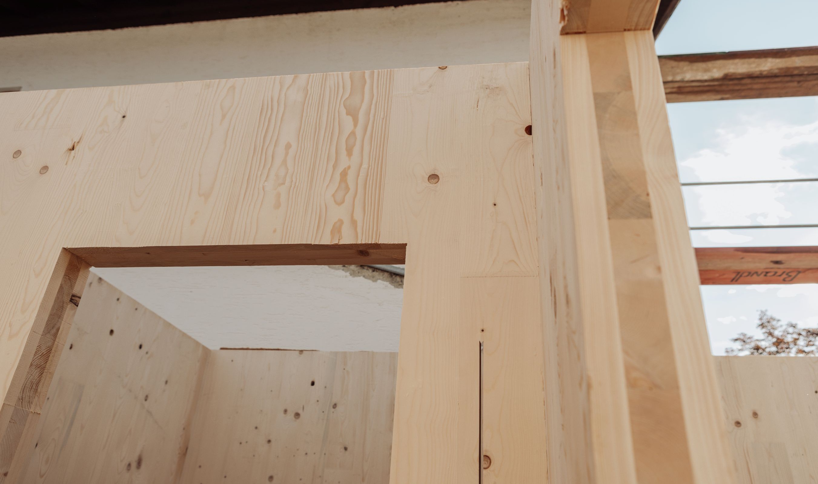 Außenansicht der Baustelle mit montierten Brettsperrholzwänden des Anbaus und Baustelleneinrichtung im Vordergrund.