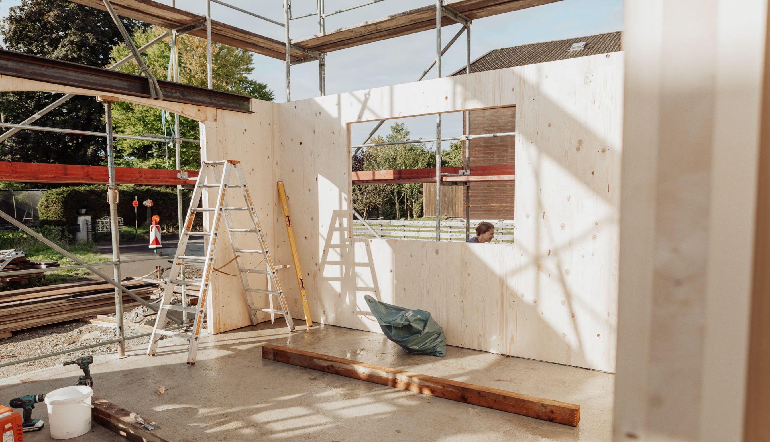 Außenansicht der Baustelle mit montierten Brettsperrholzwänden des Anbaus und Baustelleneinrichtung im Vordergrund.