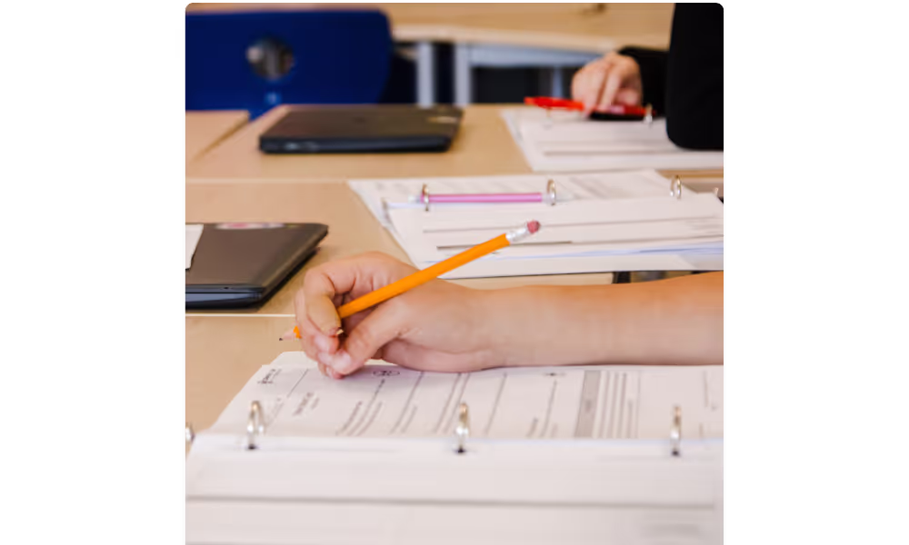 Students' hands writing in workbooks in class
