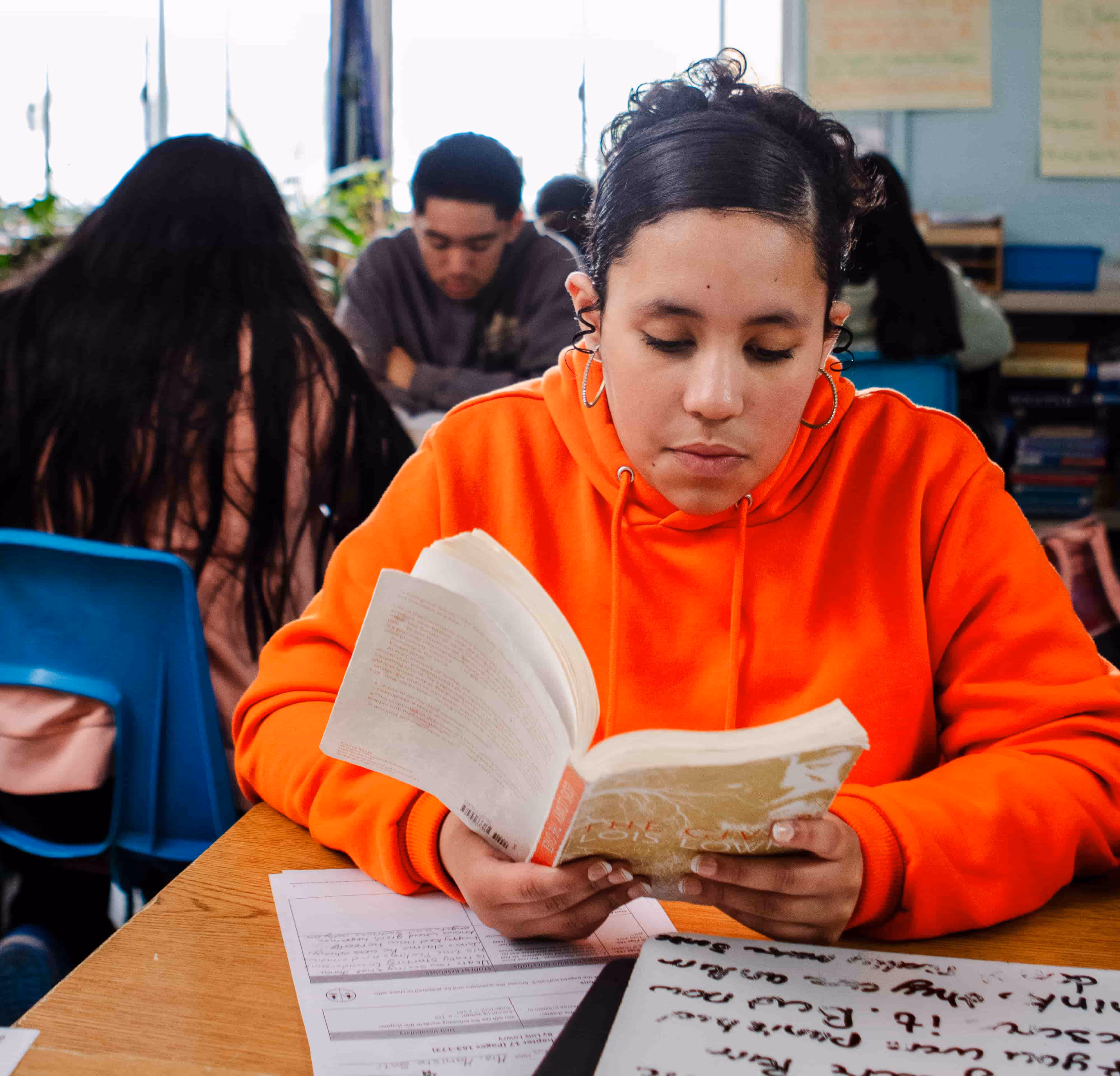 Student reading from a book at her desk in a classroom