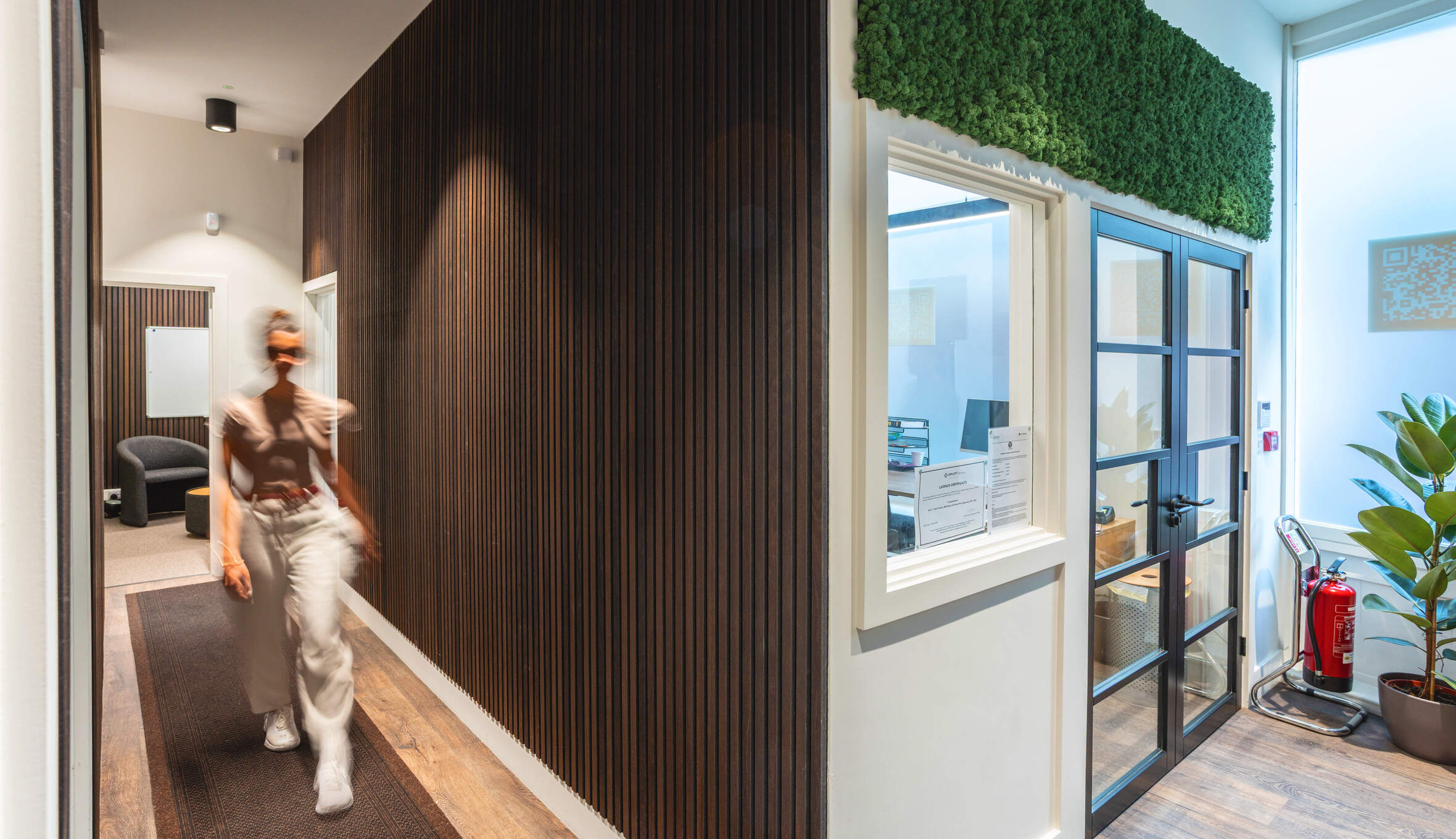 Entrance with curved timber slats, wood flooring, and a person walking through a light-filled, natural-toned space.