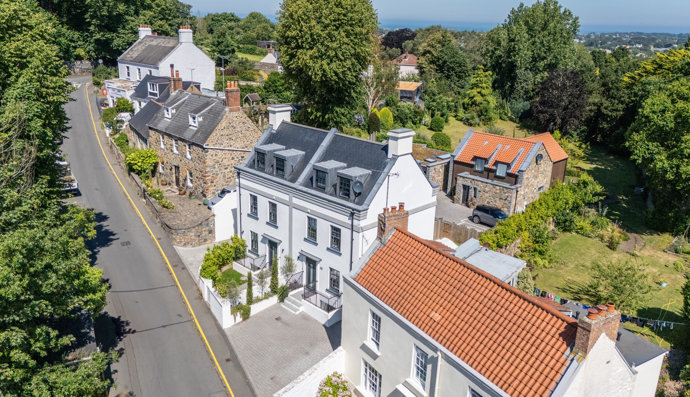 Aerial view of charming street with white and stone houses, slate and red-tiled roofs, and lush gardens