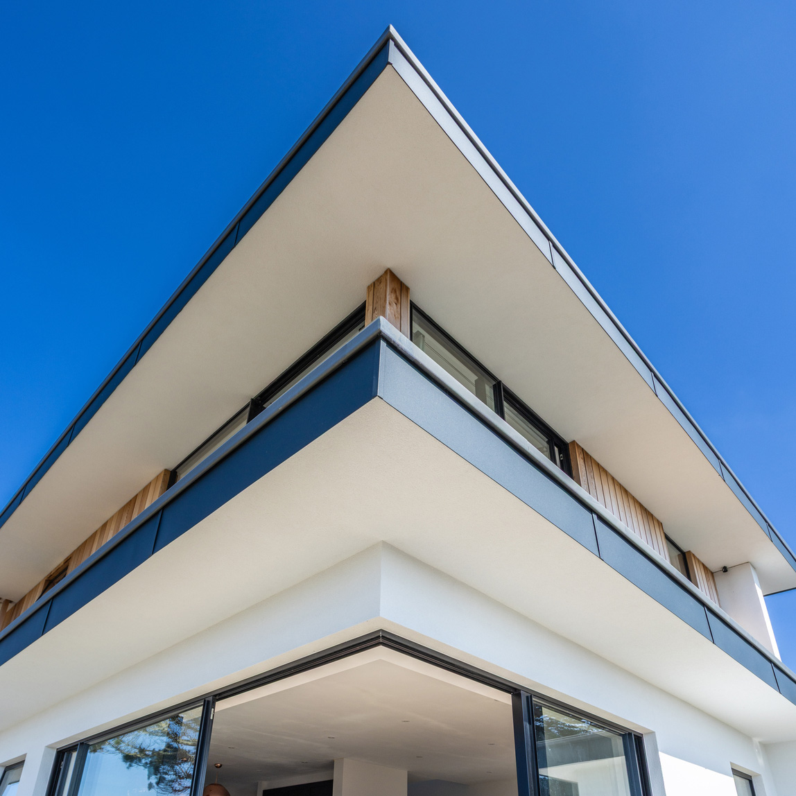 Modern two-story home with sleek lines, large windows, and a cantilevered roof against a clear blue sky.