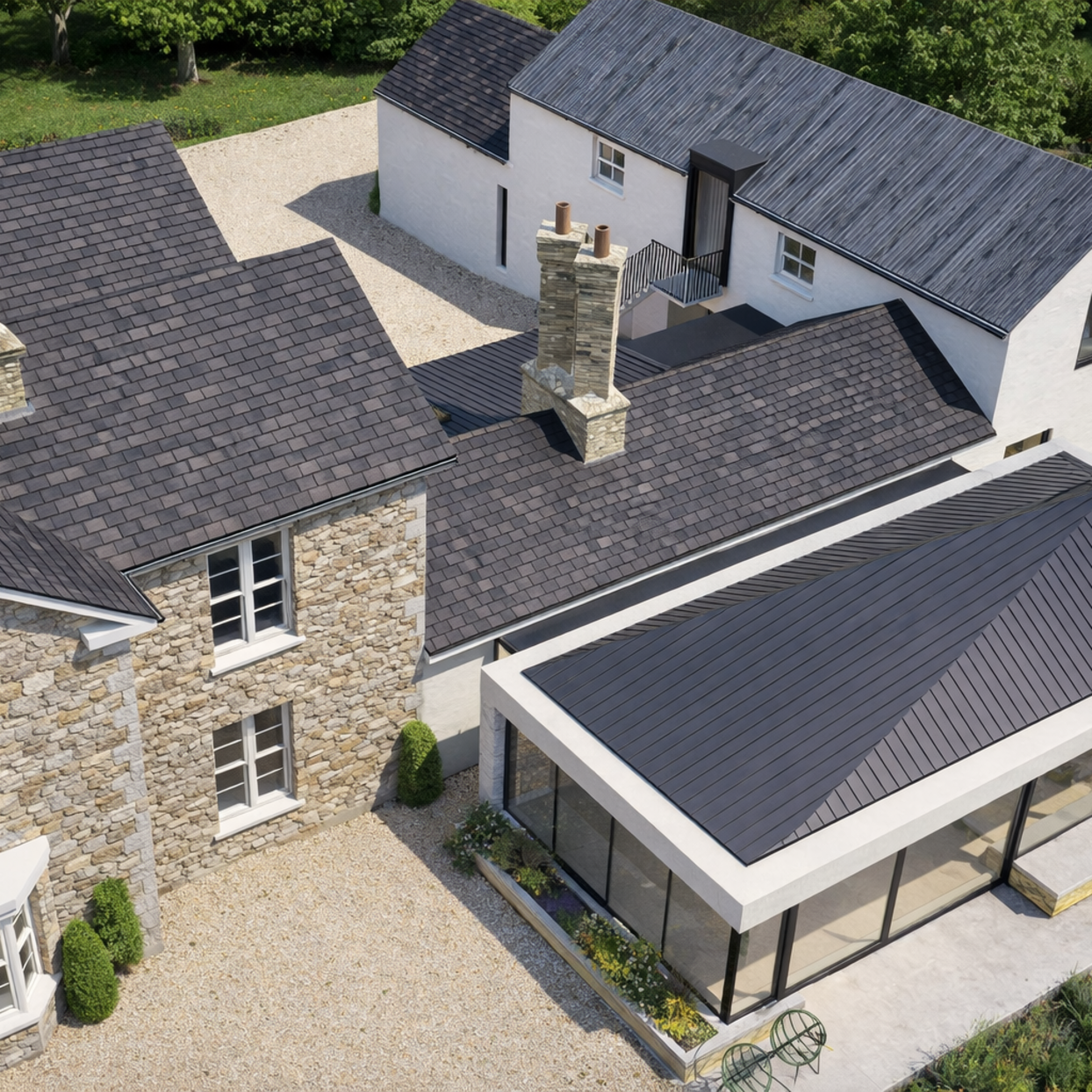 An aerial view of a traditional stone house with dark roofs and white contemporary extensions, with glazed modern extension