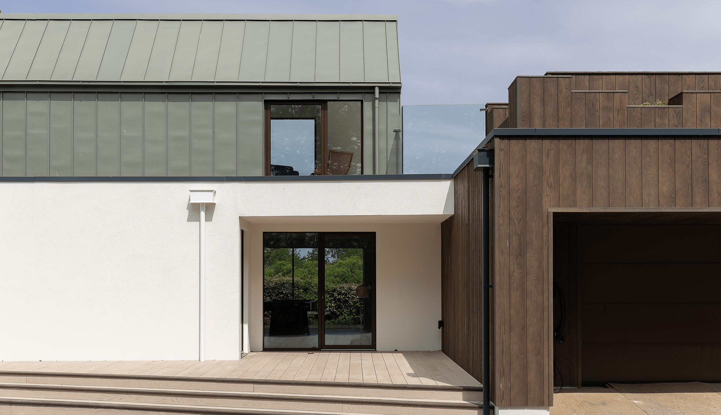 Contemporary home exterior with white render, zinc metal cladding and dark timber garage.