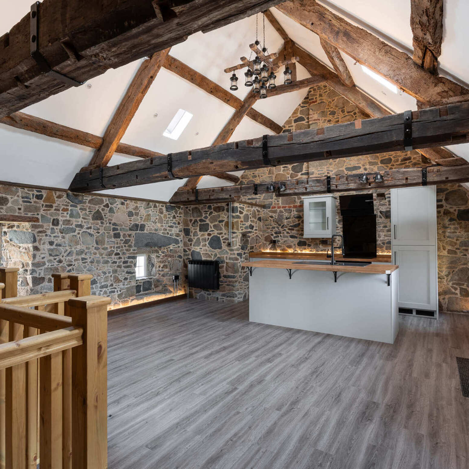Rustic loft interior with exposed timber beams, stone walls, modern kitchen island, and wood flooring.