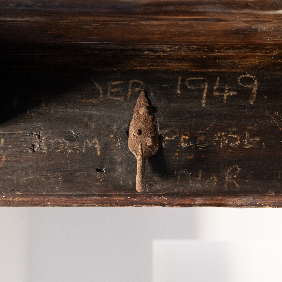 Rusty metal latch on a weathered wooden beam, with faint numbers and letters scratched into the wood surface.