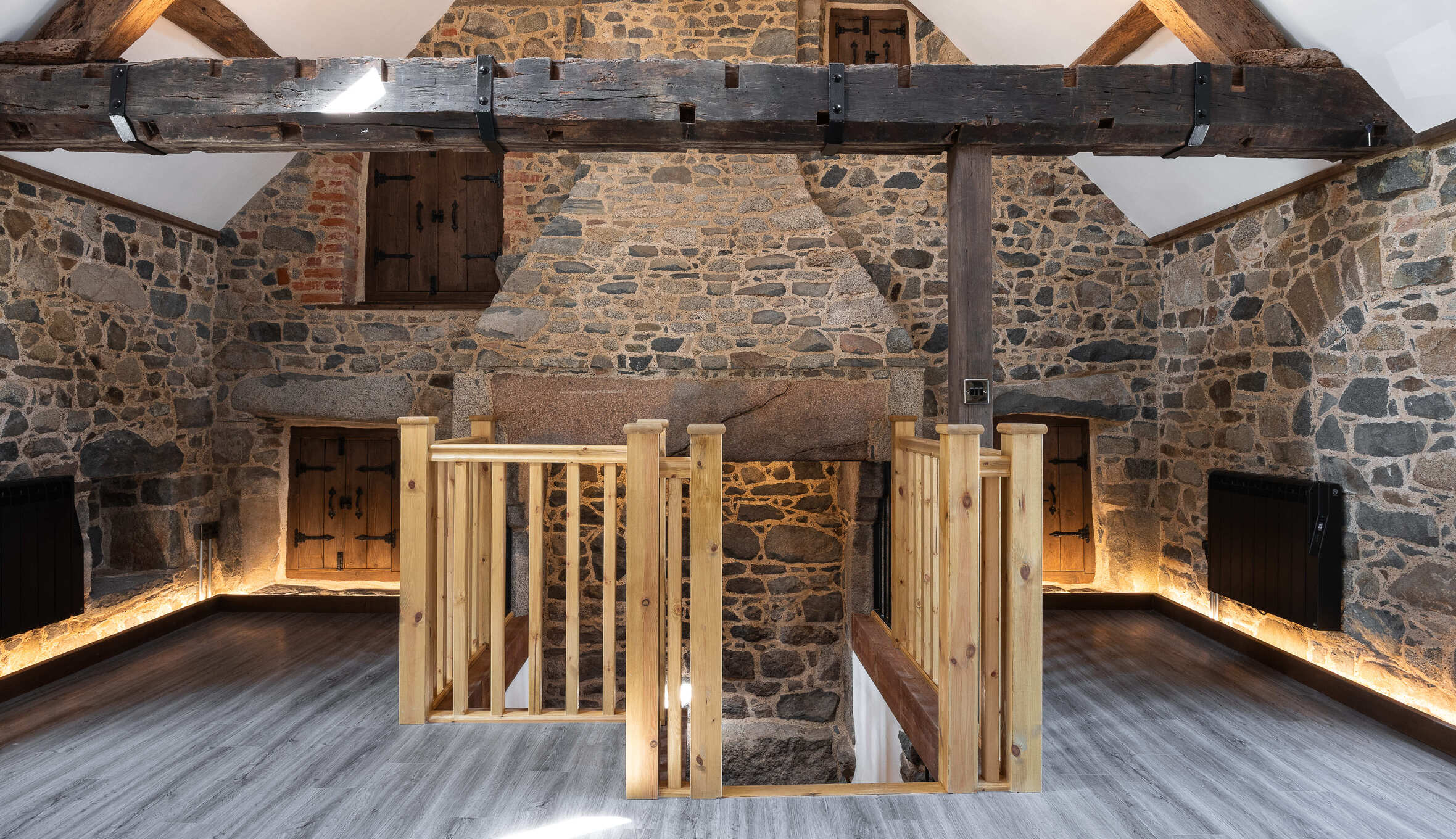 Stone loft landing with wooden railings, exposed beams, built-in cupboards, and warm lighting detail.