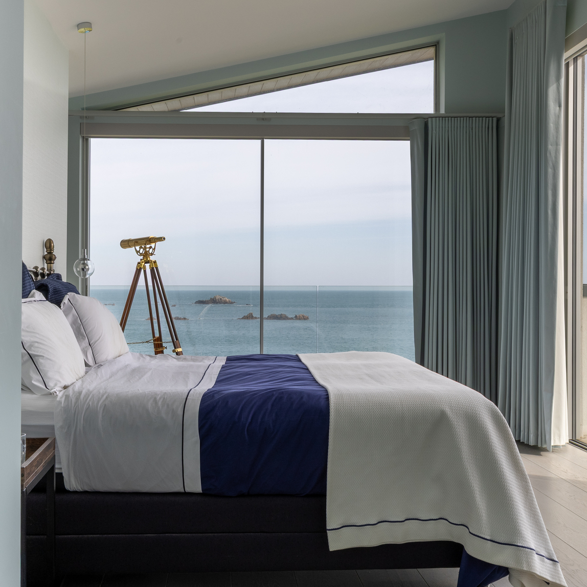 Coastal bedroom with ocean views, a brass telescope, and white and navy bedding.