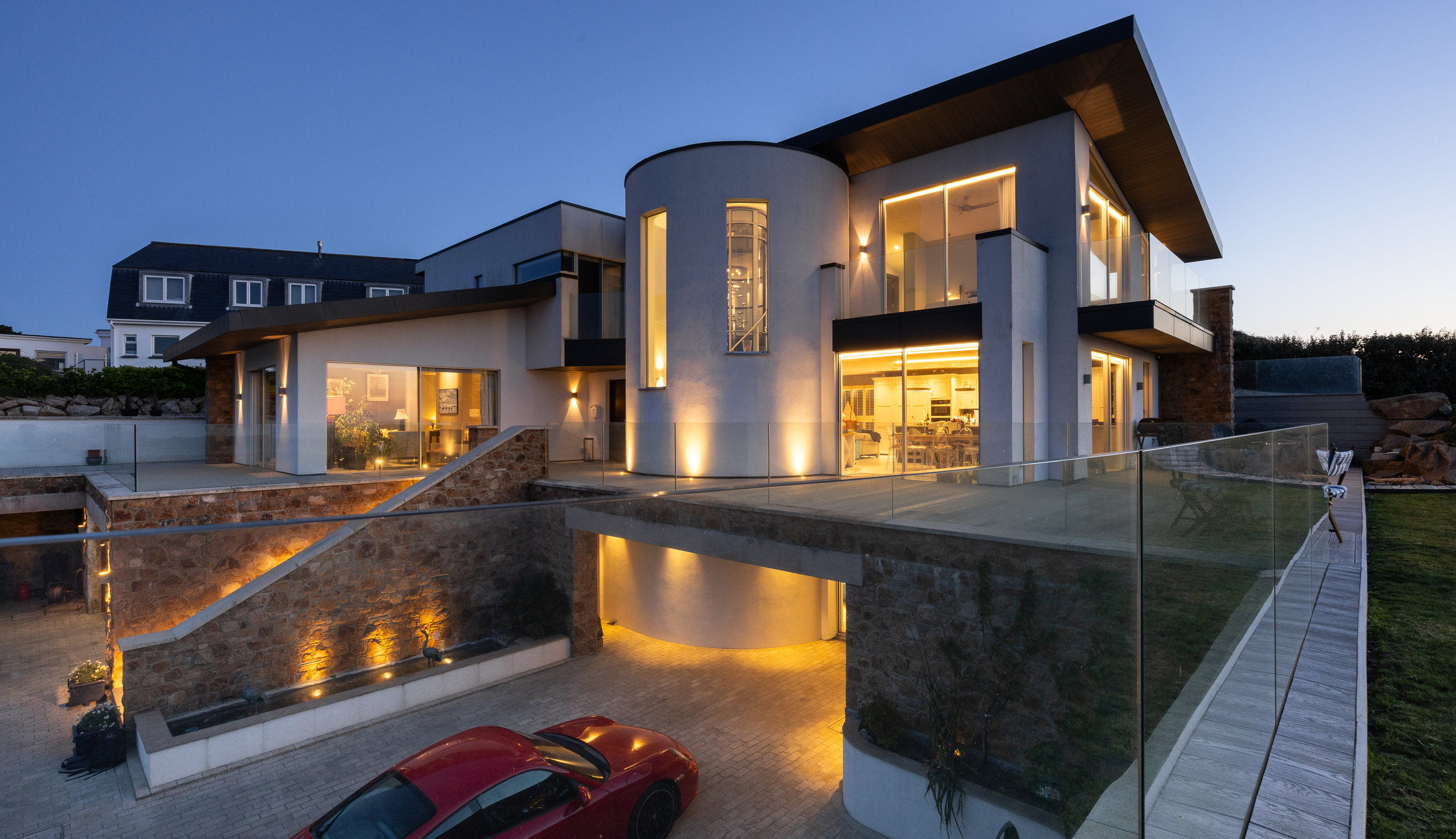 Modern white coastal home with glass balconies and warm lighting at dusk.