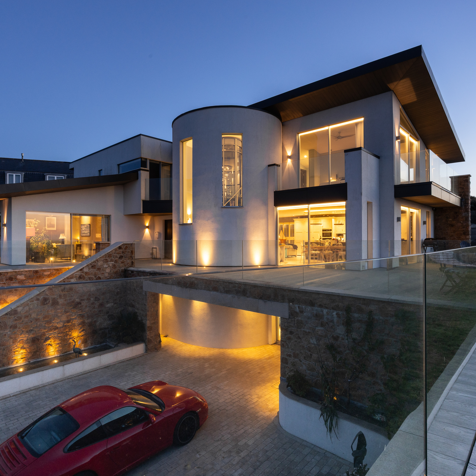 Modern white coastal home with glass balconies and warm lighting at dusk.