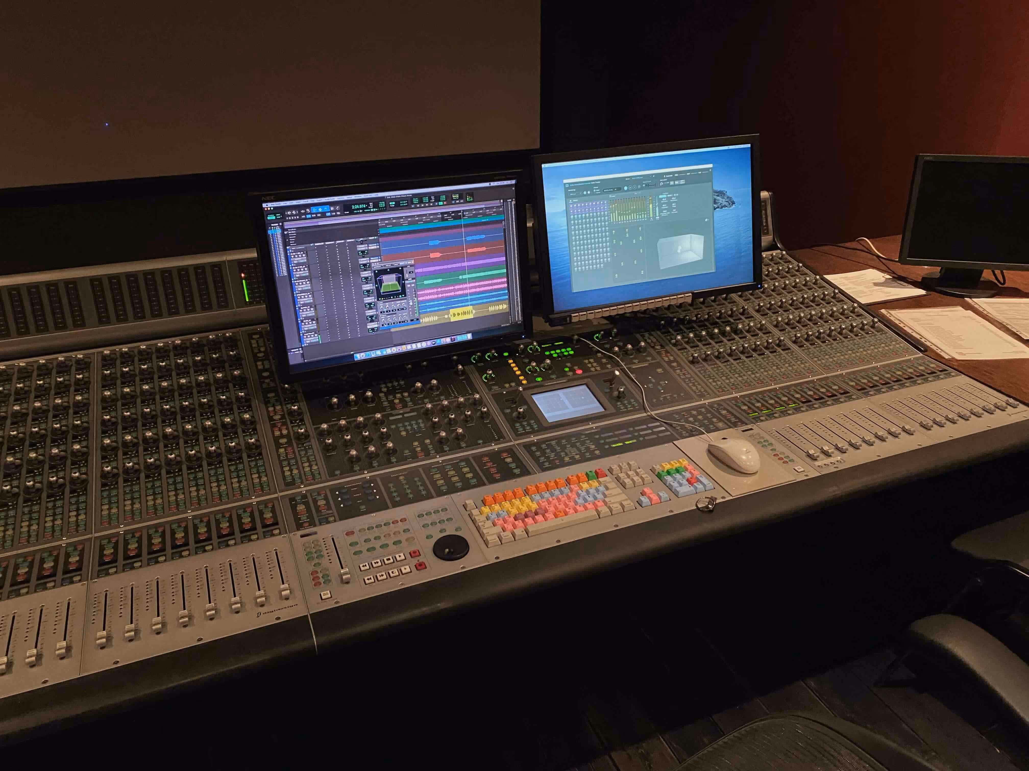 Professional mixing console and Dolby Atmos studio setup featuring dual monitors displaying a digital audio workstation (DAW) interface and surround sound panning tools, highlighting a state-of-the-art environment for precise music mixing and mastering.