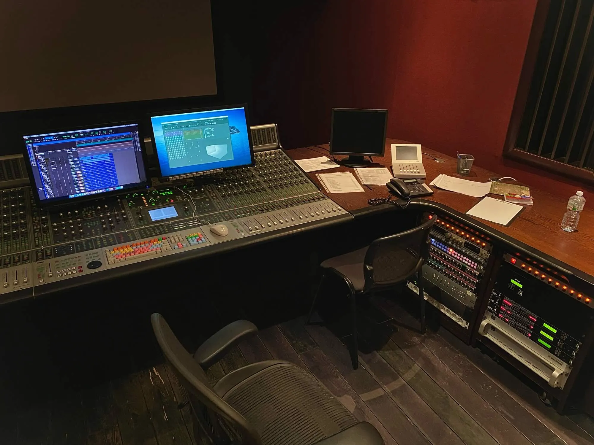 Comprehensive view of a Dolby Atmos mixing studio featuring a professional mixing console, dual monitors with a digital audio workstation (DAW) interface, outboard gear, and a workspace with notes and equipment, illustrating a well-equipped environment for precision audio production.