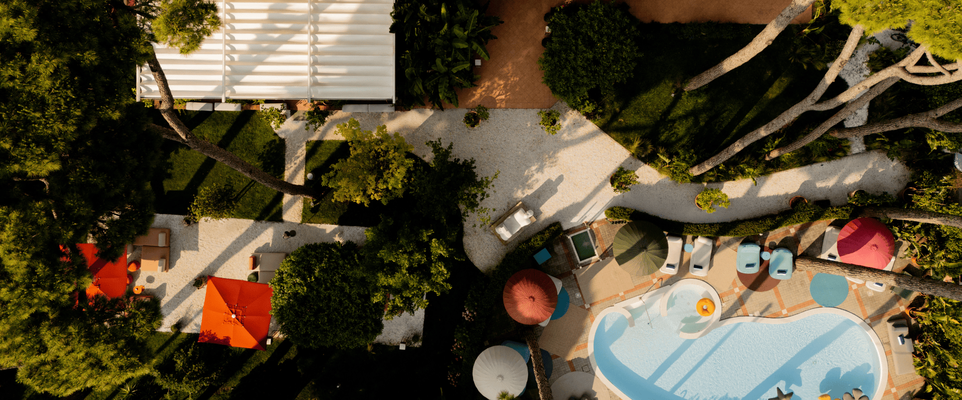 Top-down shot of Serena Hotel Tuscany outdoor swimming pool surrounded by pine trees, gravel walkways, and terrace seating