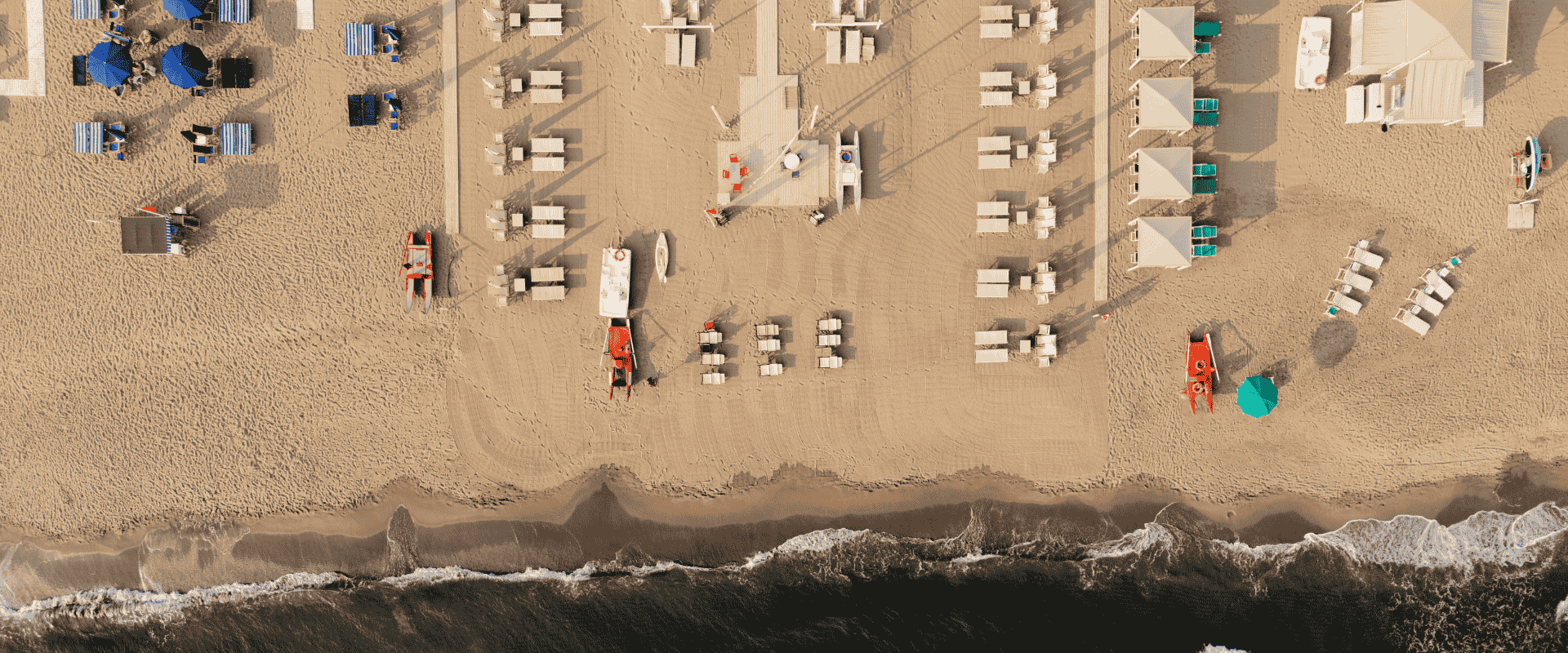Top-down drone shot of a Tuscany beach resort with organized deck chairs, cabanas, and shoreline by the sea