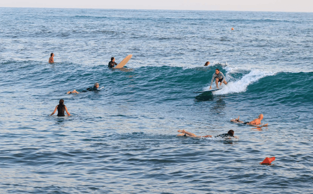 Surfisti che cavalcano le onde con altri che nuotano e aspettano nell'oceano