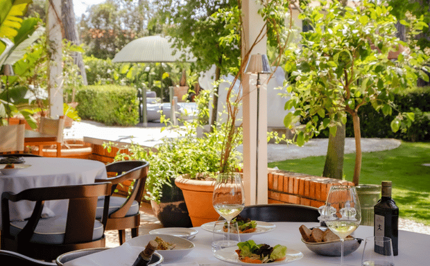 Elegante terrazza di ristorante all'aperto con tavoli apparecchiati e vegetazione lussureggiante.