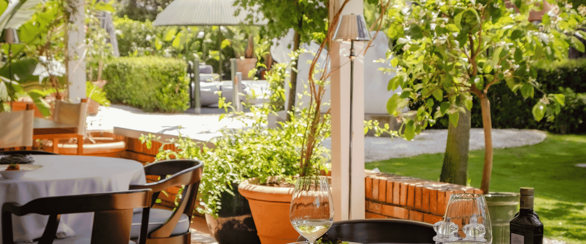 Sunny al fresco dining area featuring white tablecloths and potted plants.