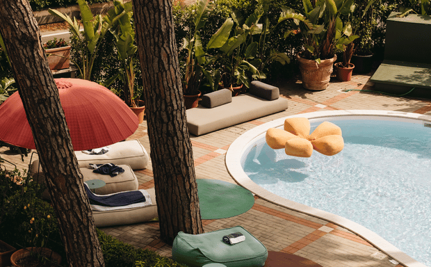 Piscina curva con un galleggiante a forma di fiore giallo circondata da cuscini prendisole.
