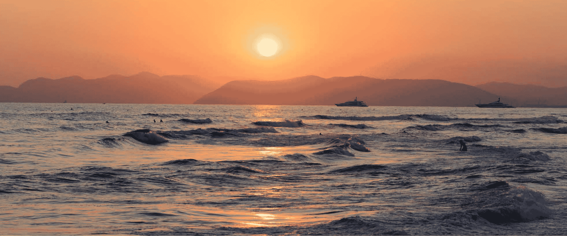 Sun setting behind mountains over the sea in Forte dei Marmi, featuring boats on the horizon.